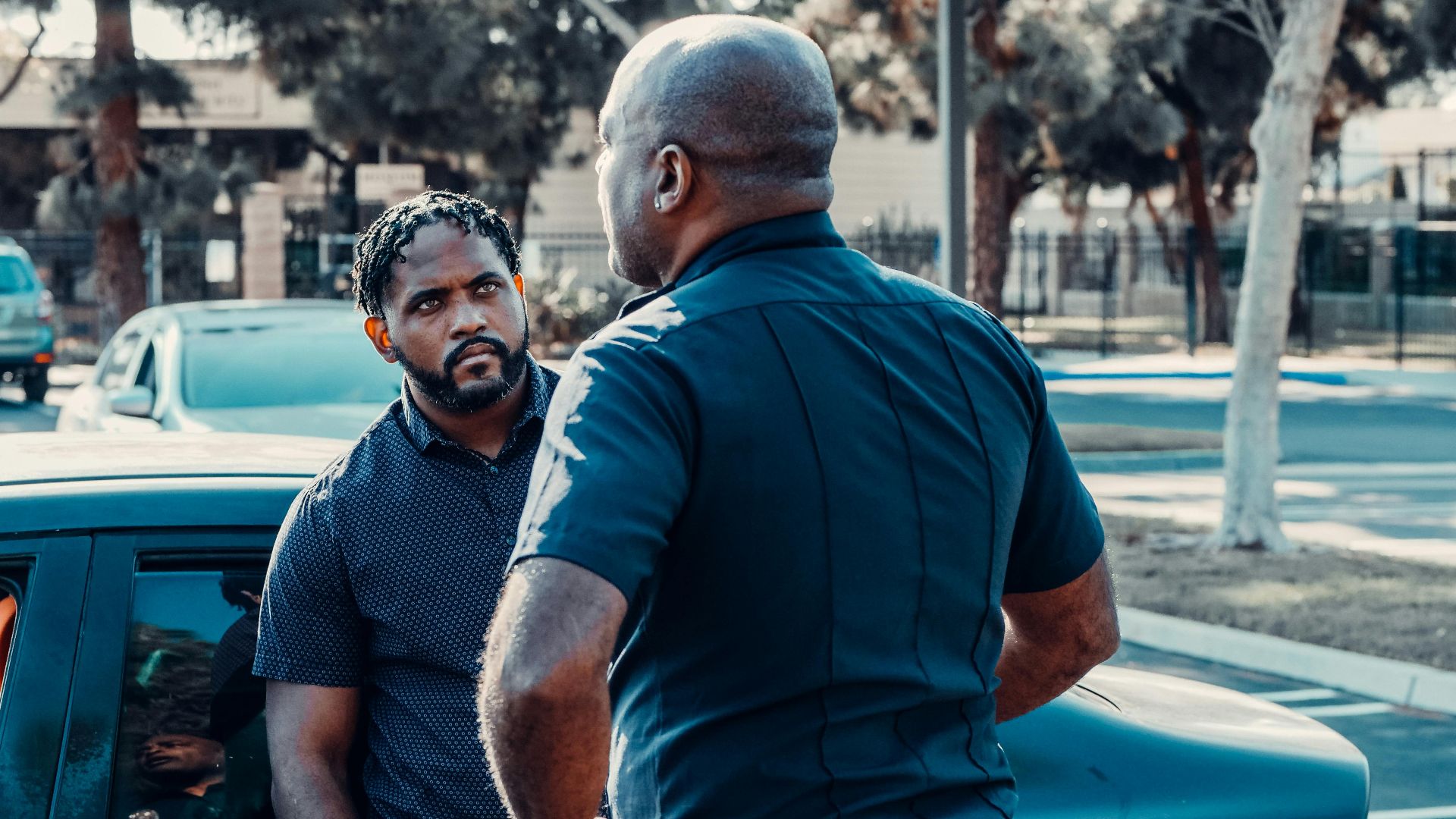 A police officer talking to a man beside a car on a sunny street.