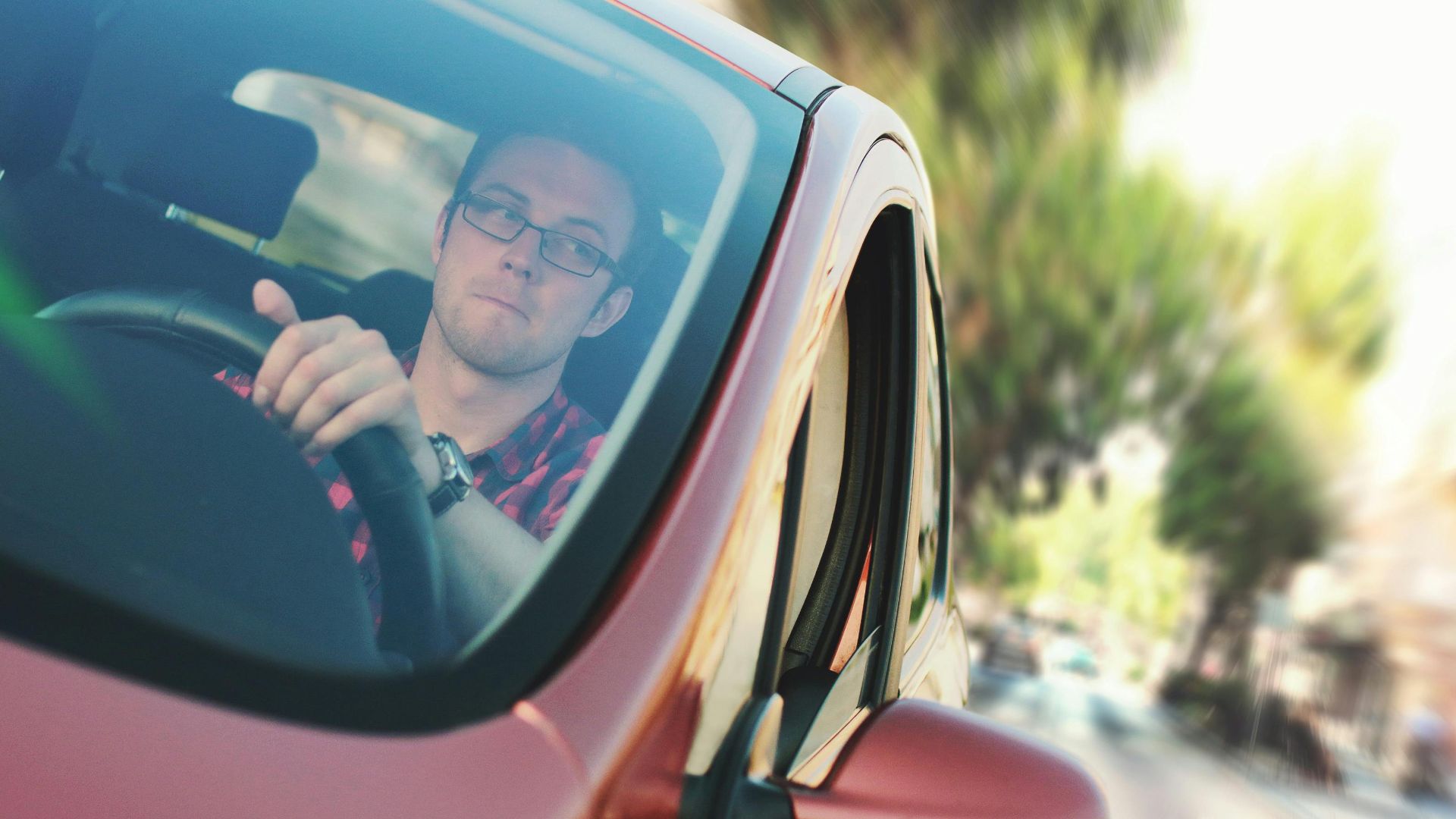 A man driving fast through a city street in a red car, showcasing motion and focus.
