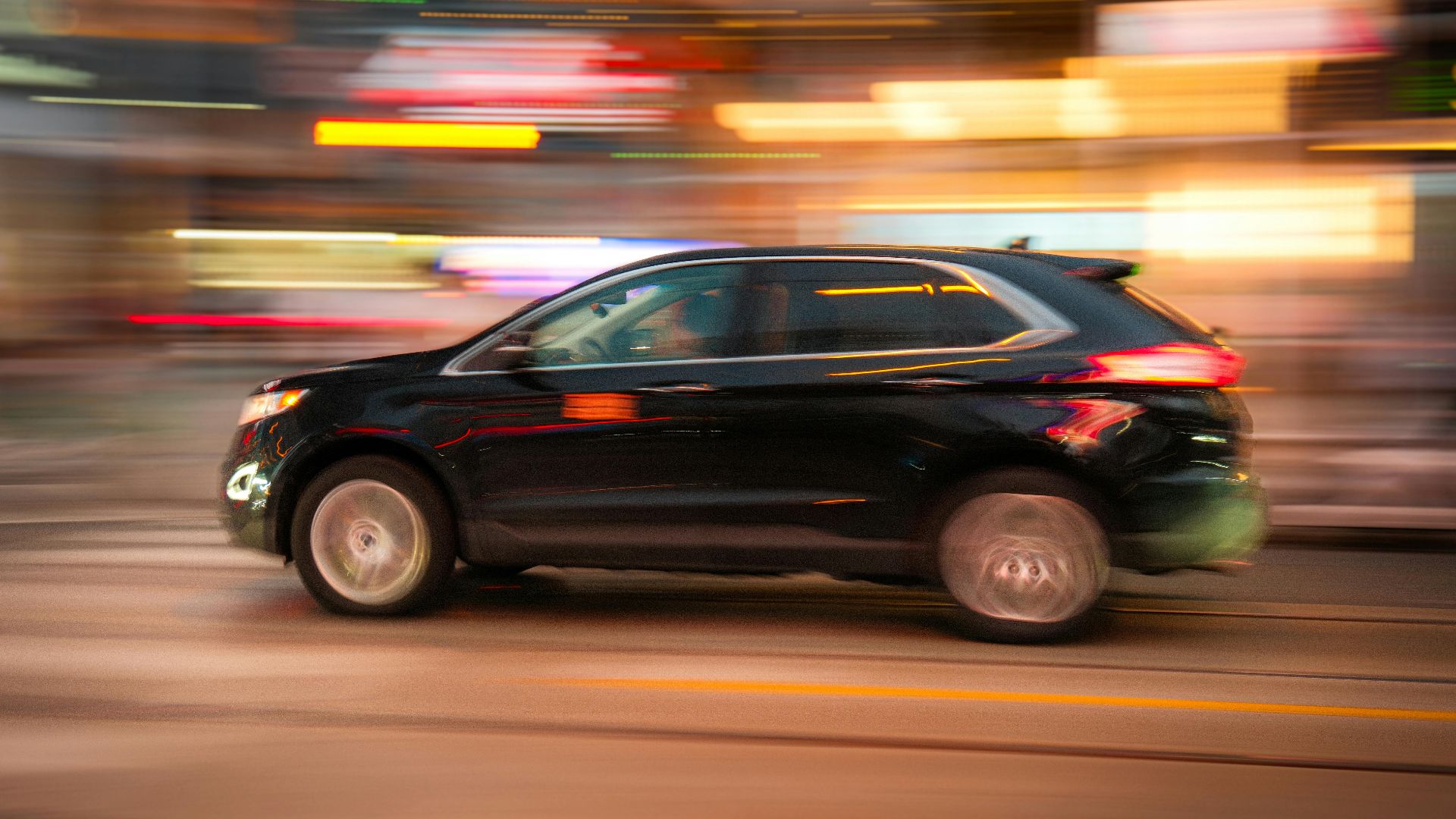 Black SUV in motion with urban background, conveying speed and city life.