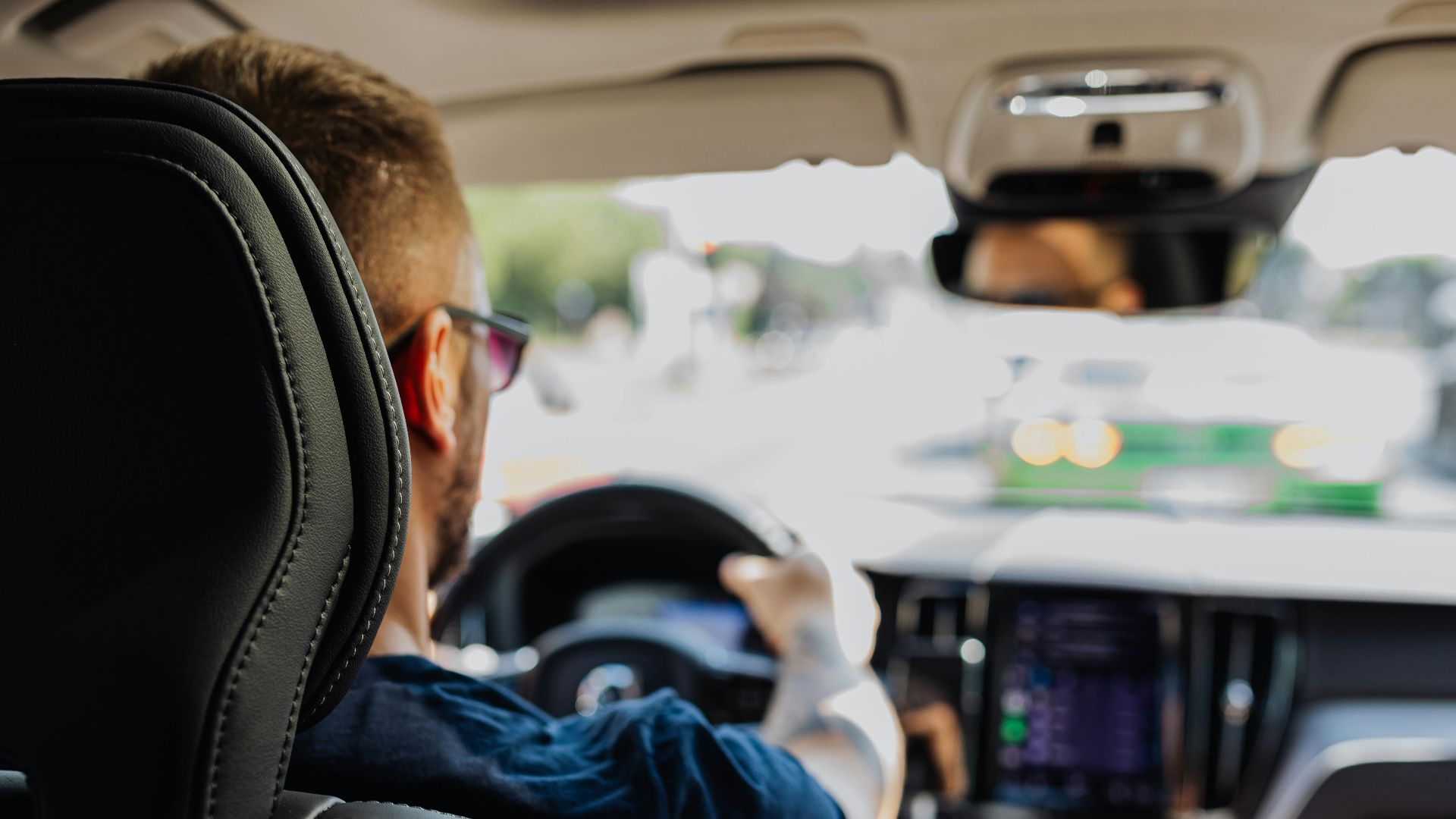 Close-up of a man driving a modern vehicle from behind with a blurred urban background.