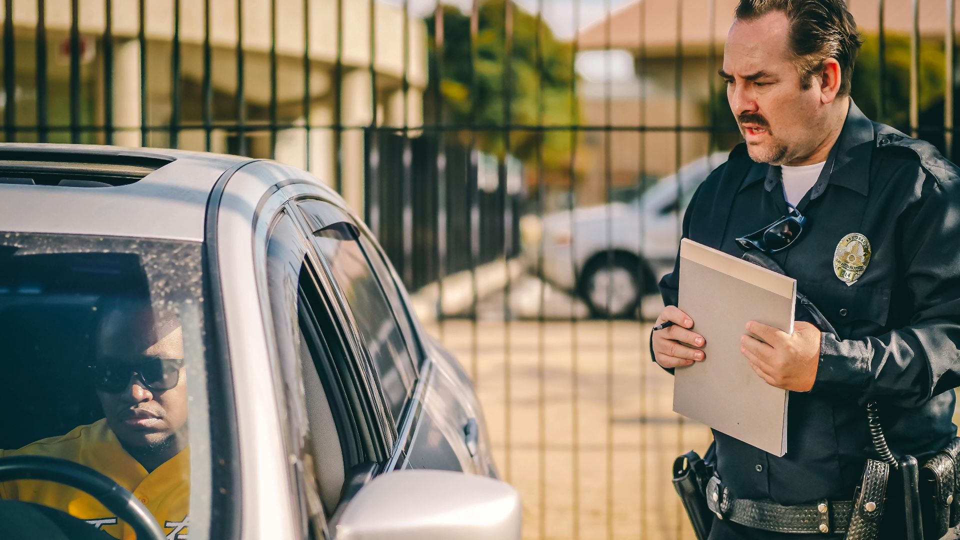 Police officer at car window issuing a ticket to a driver in a sunny outdoor setting.