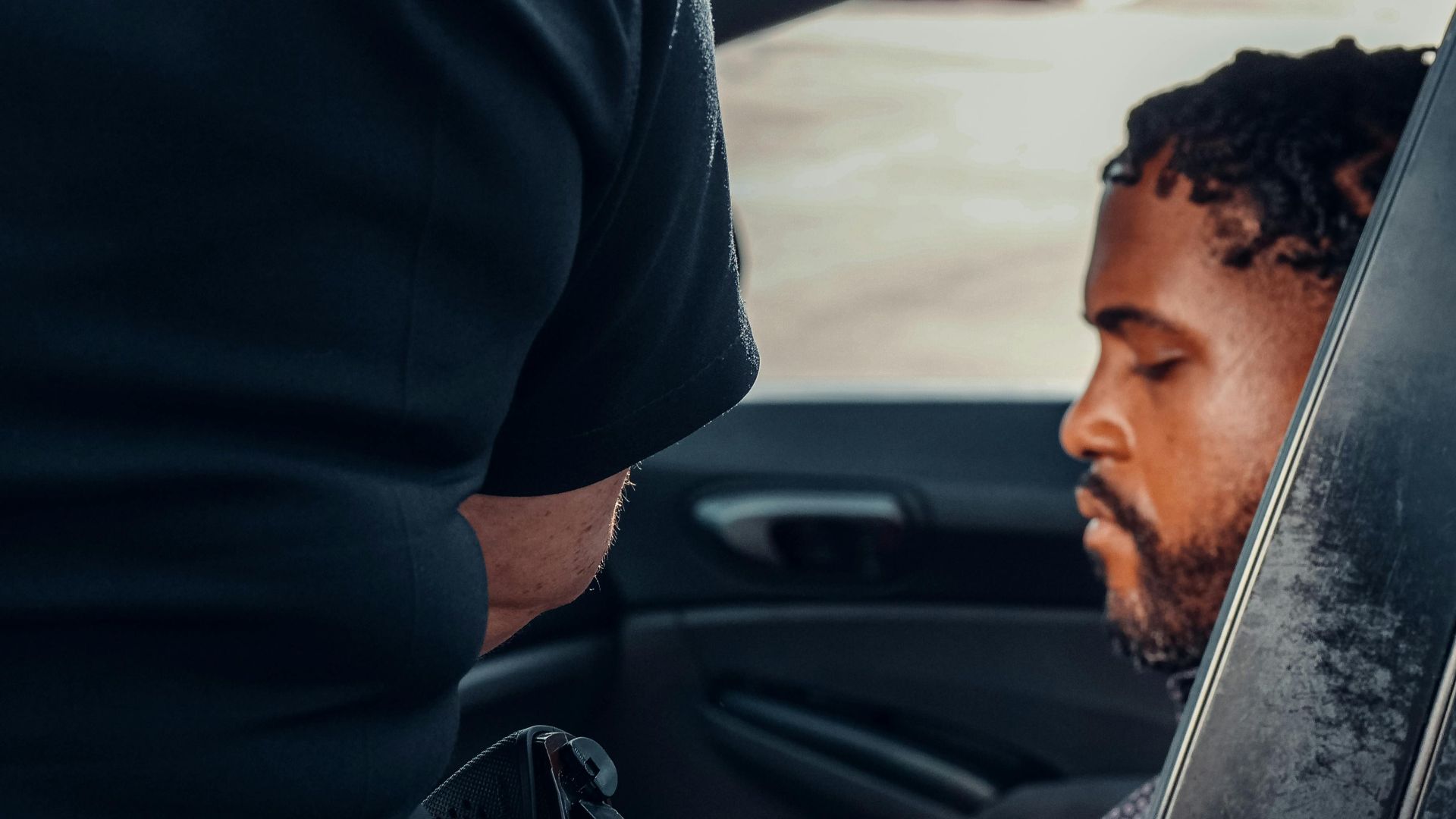 Police officer inspecting a vehicle with driver seated inside, sunny day.