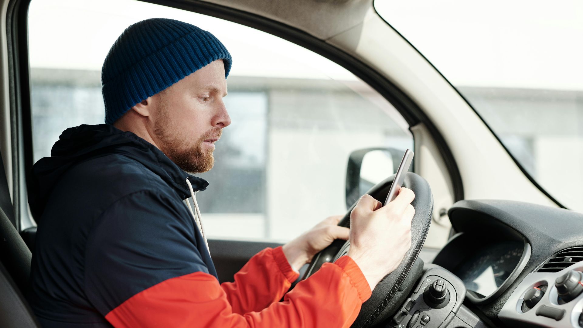 Distracted driver uses a smartphone in a car, highlighting road safety concerns.