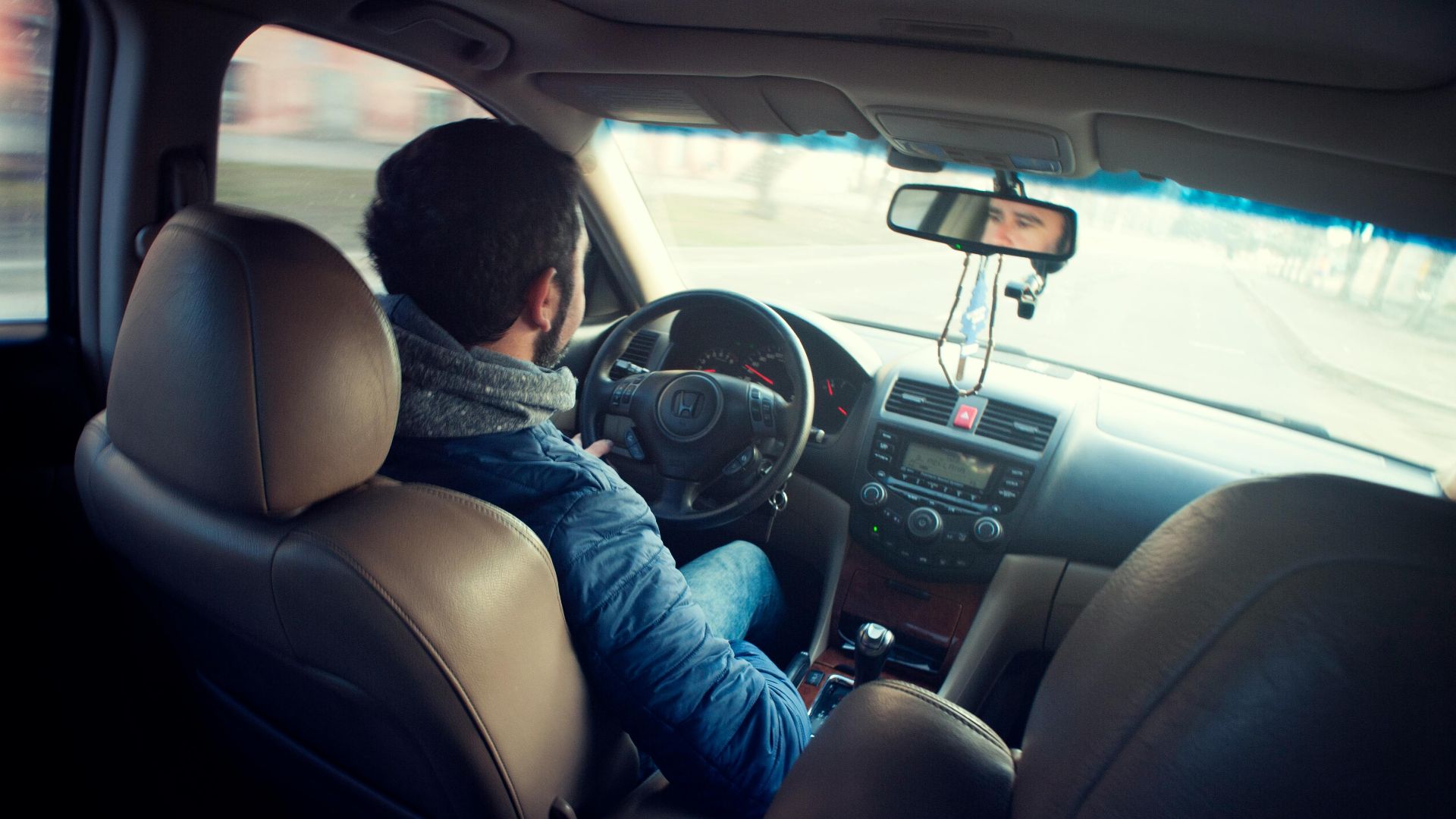 A man driving a car with focus on interior, dashboard, and steering wheel, captured from the backseat.