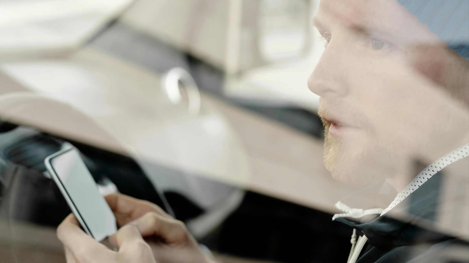 Side view of a man using a smartphone inside a car, reflecting modern technology and daily life themes.