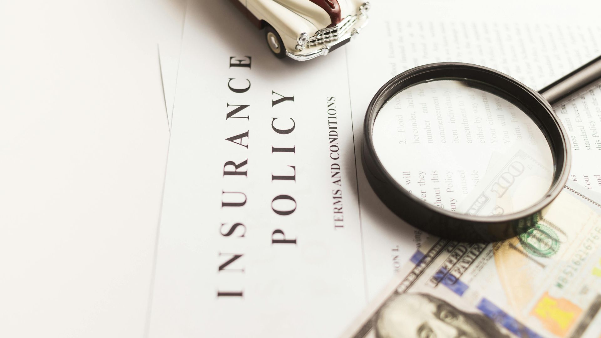 Close-up image of an insurance policy with a magnifying glass, money, and toy car.