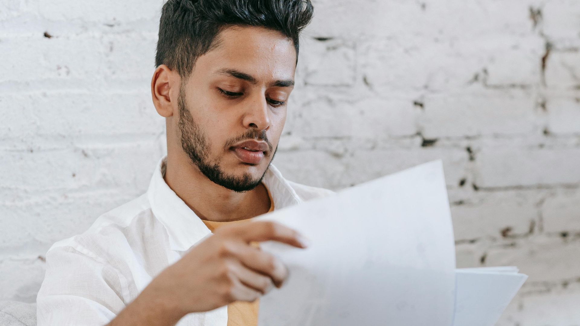 Concentrated young bearded Hispanic male sitting in armchair and analyzing contract while getting job offer