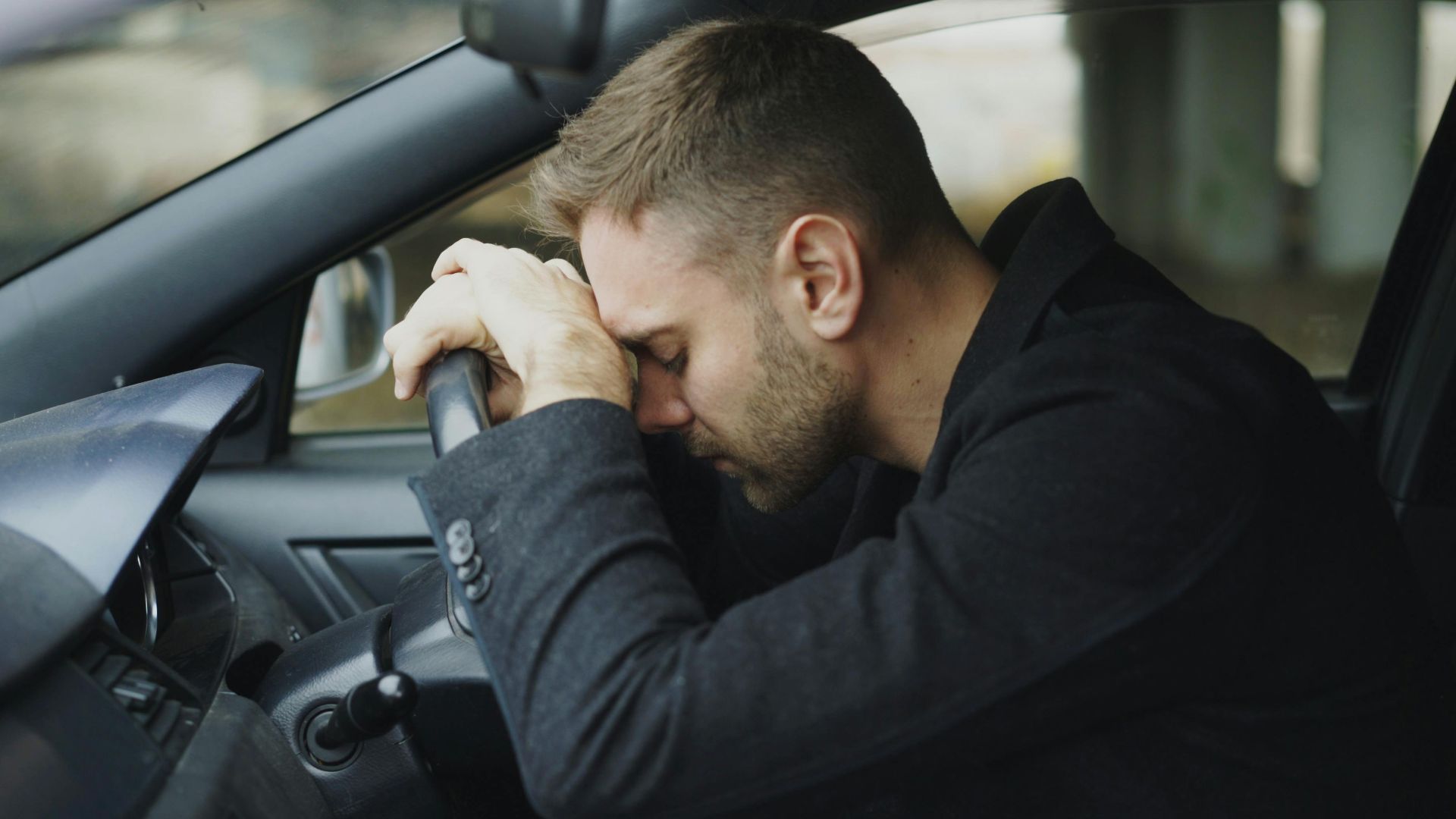 A man showing stress while sitting in a car, head on steering wheel.