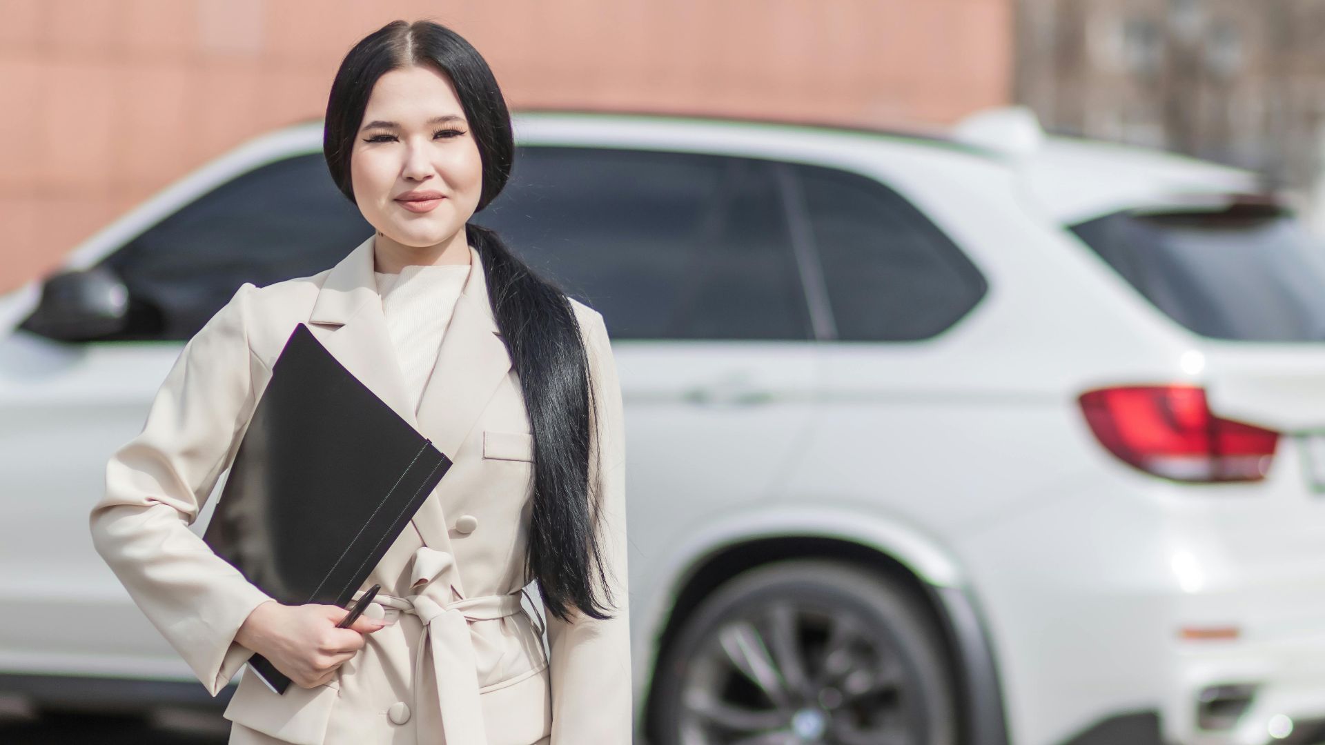 Smiling professional woman standing confidently by a luxury car, embodying success.