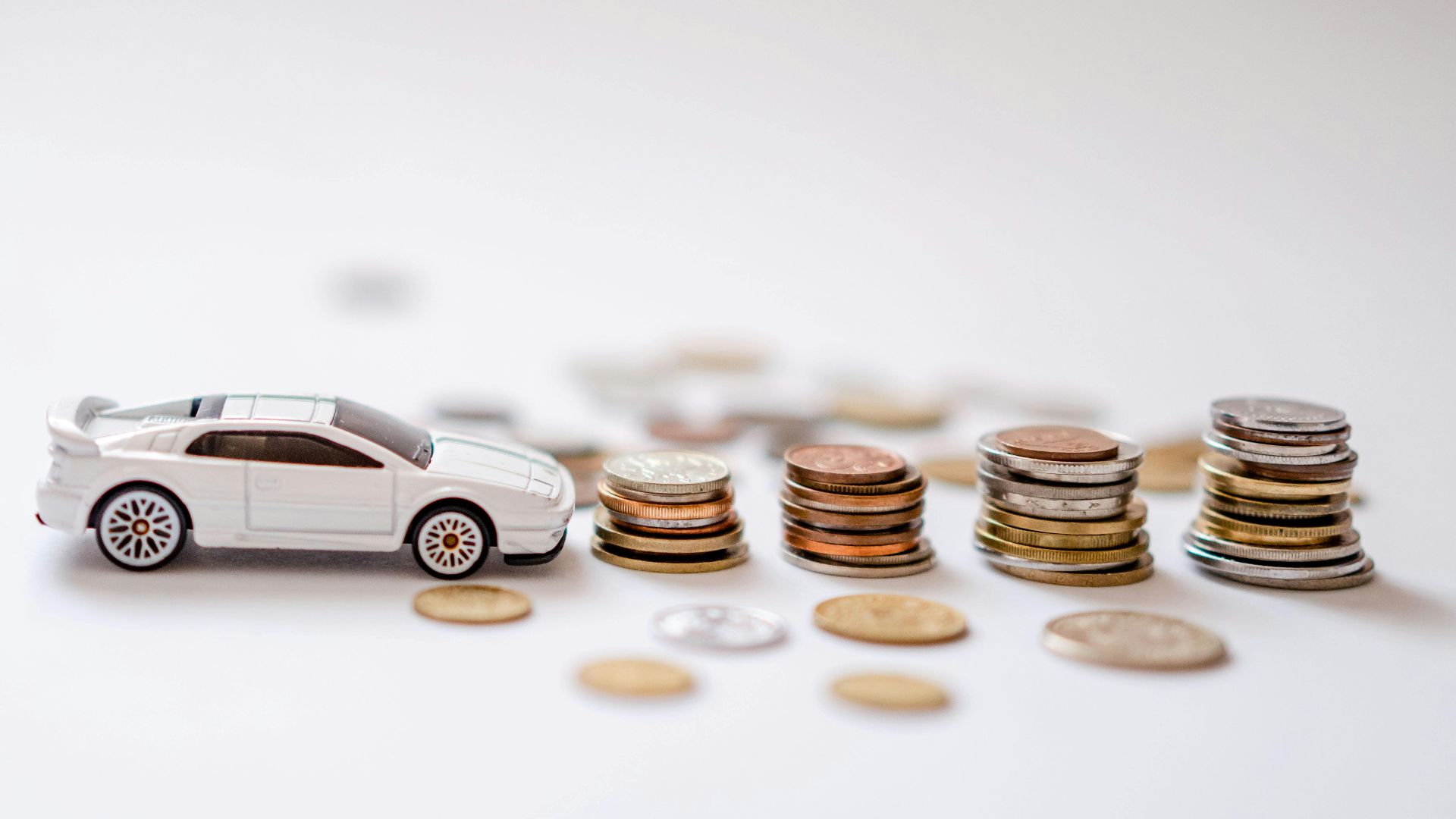 White toy sports car beside stacks of coins on a white background, emphasizing savings and finance.