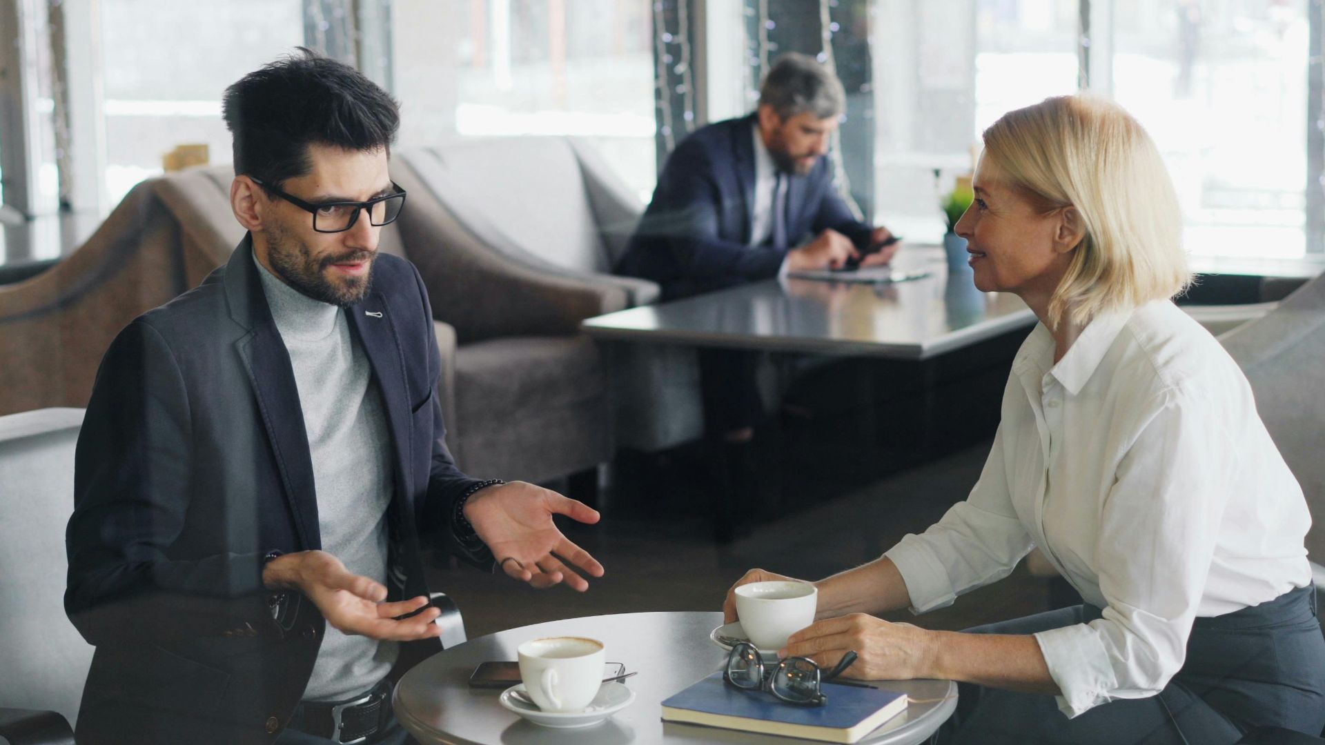 Professional colleagues discuss work over coffee in a contemporary café setting.