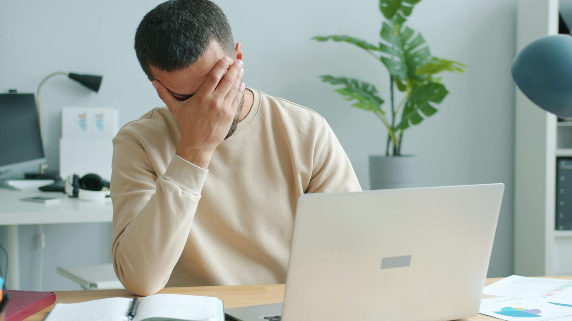 Young man overwhelmed at his desk with laptop, office stress.