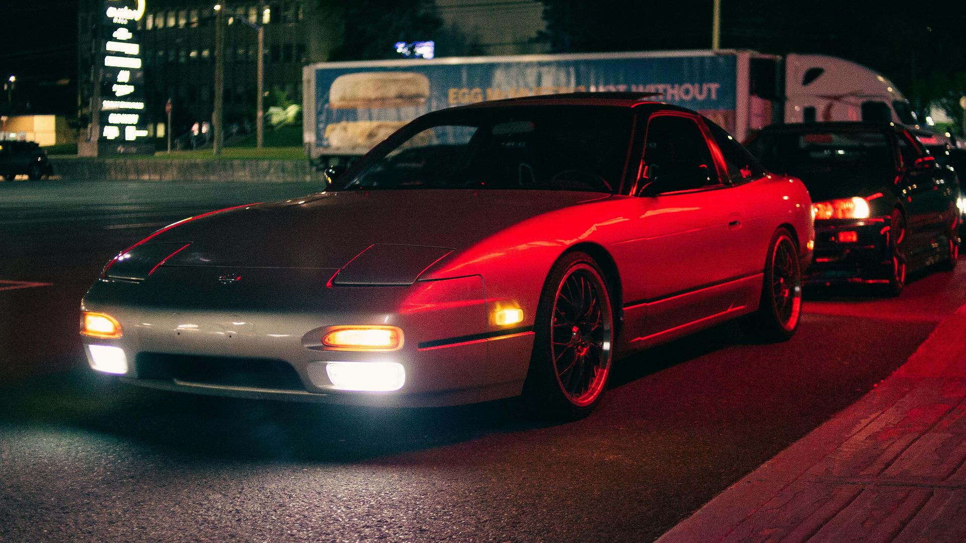 A line of stylish cars parked on a city street at night with red and white headlights creating a vivid visual.