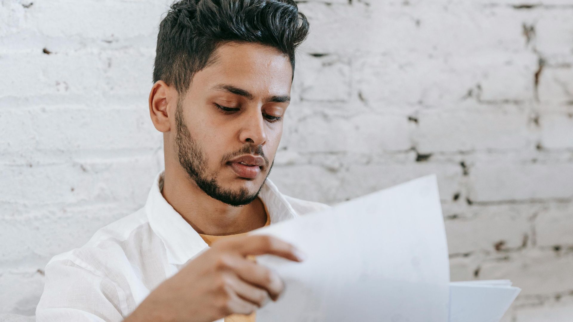 Concentrated young bearded Hispanic male sitting in armchair and analyzing contract while getting job offer