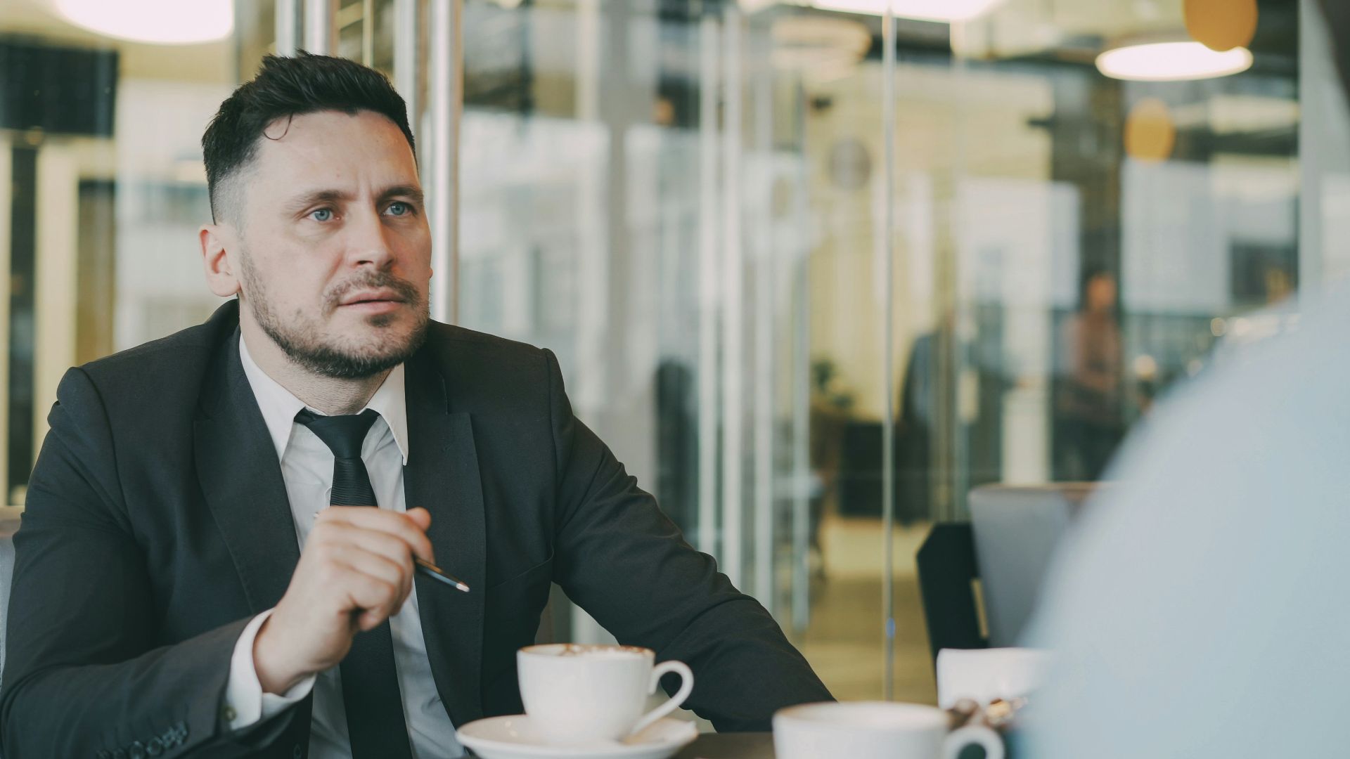 Man in suit talks at table with coffee cups.
