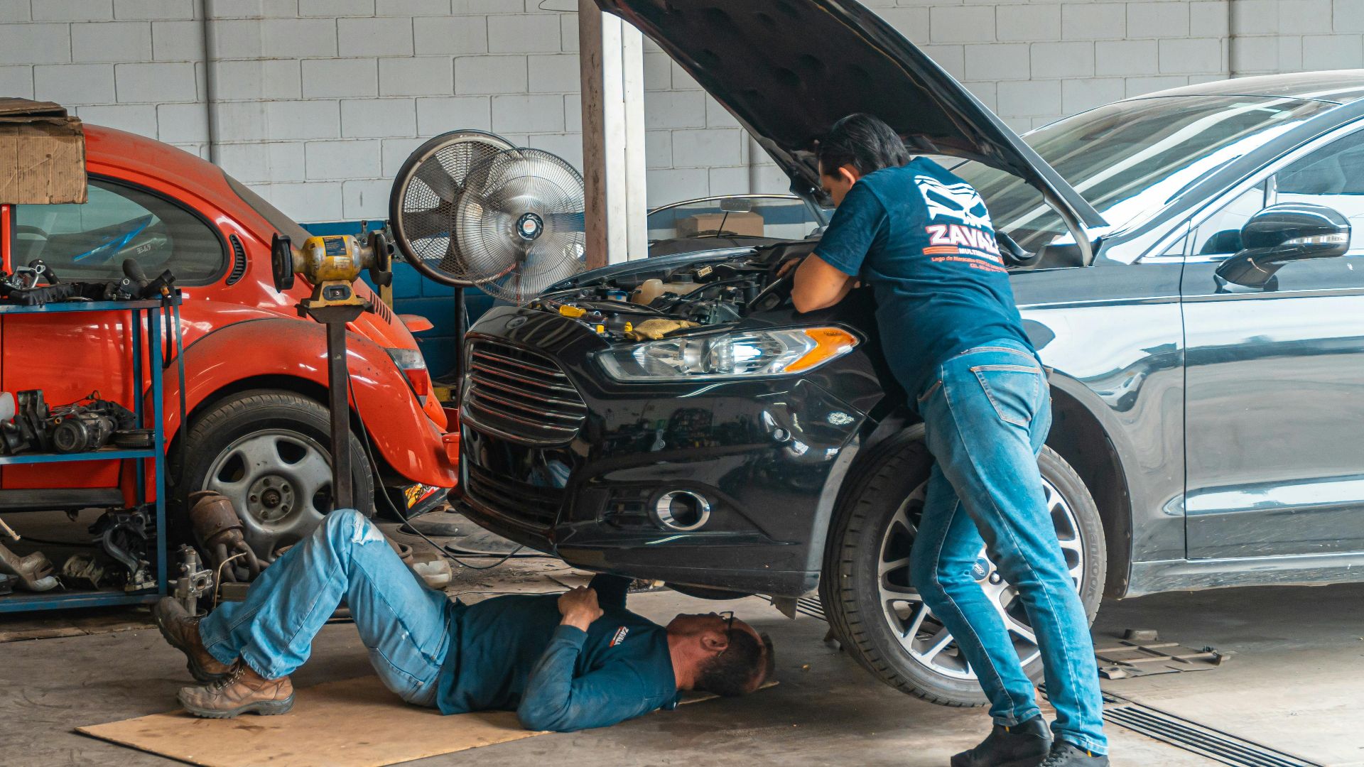 Mechanics working in an automotive workshop, repairing cars and performing maintenance.