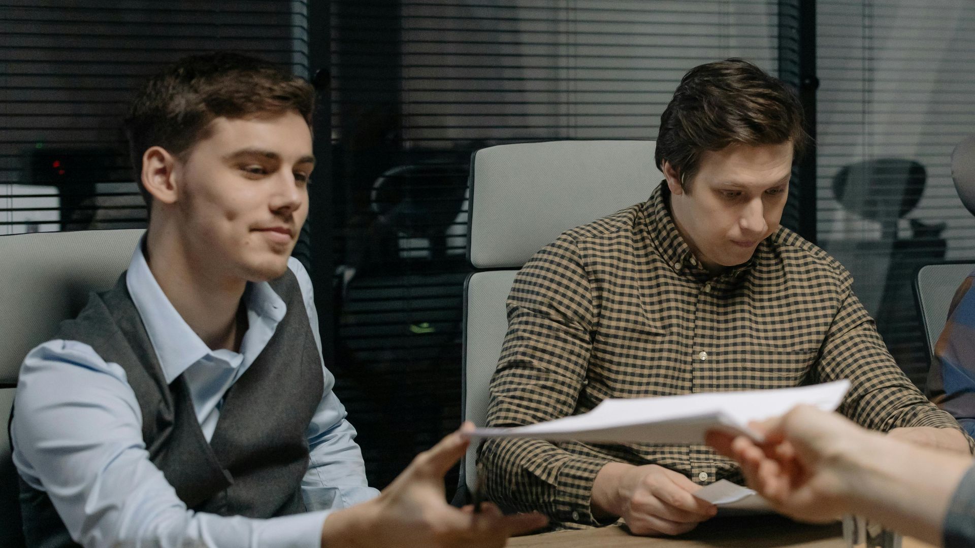 Four professionals exchanging documents during a meeting in an office setting.