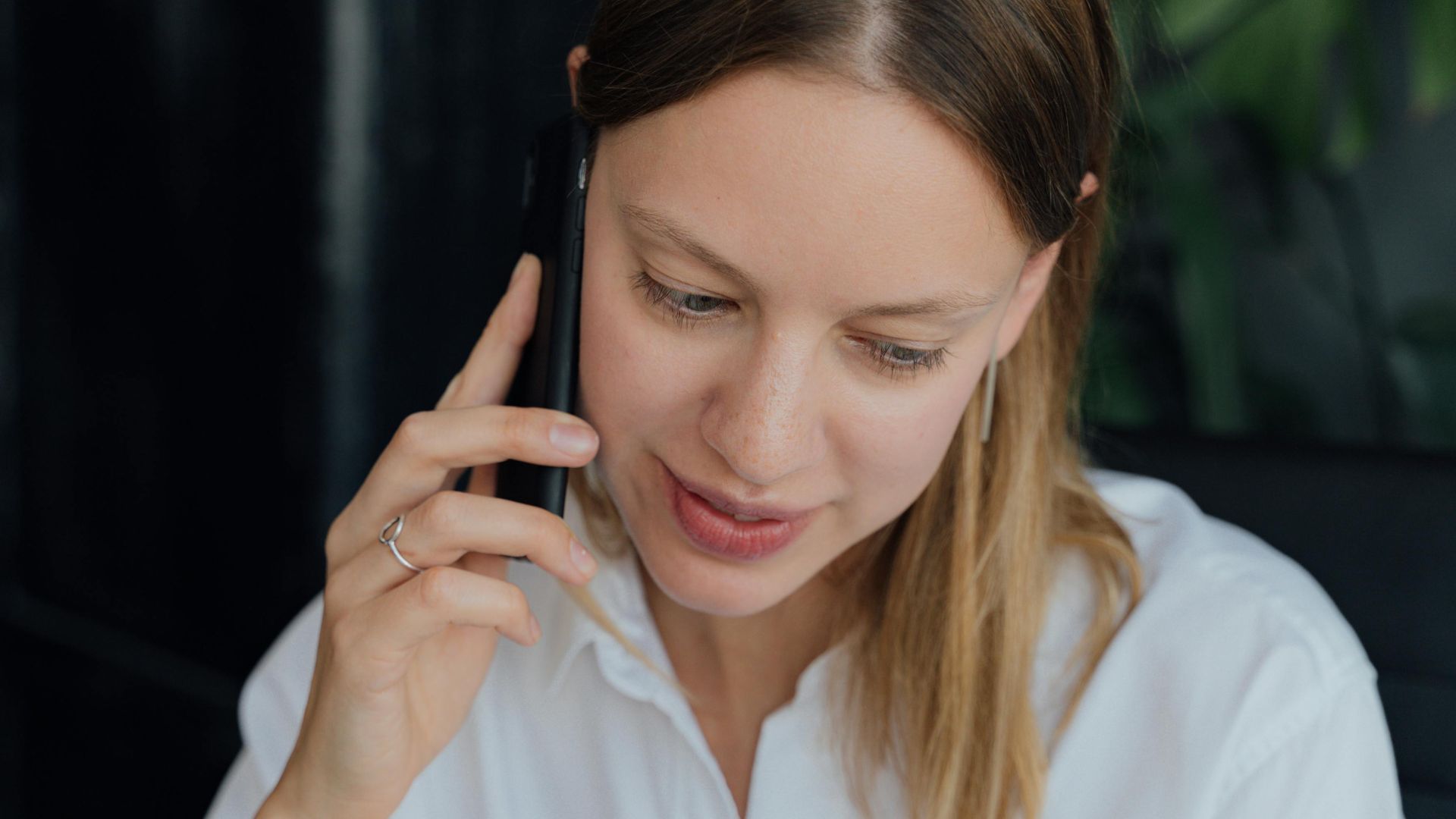 A professional woman in a white shirt making a phone call in an indoor setting, showing communication and business engagement.