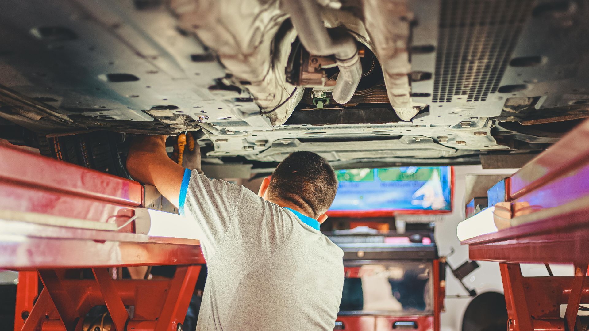 A mechanic works under a lifted car in an auto repair shop, adjusting parts.