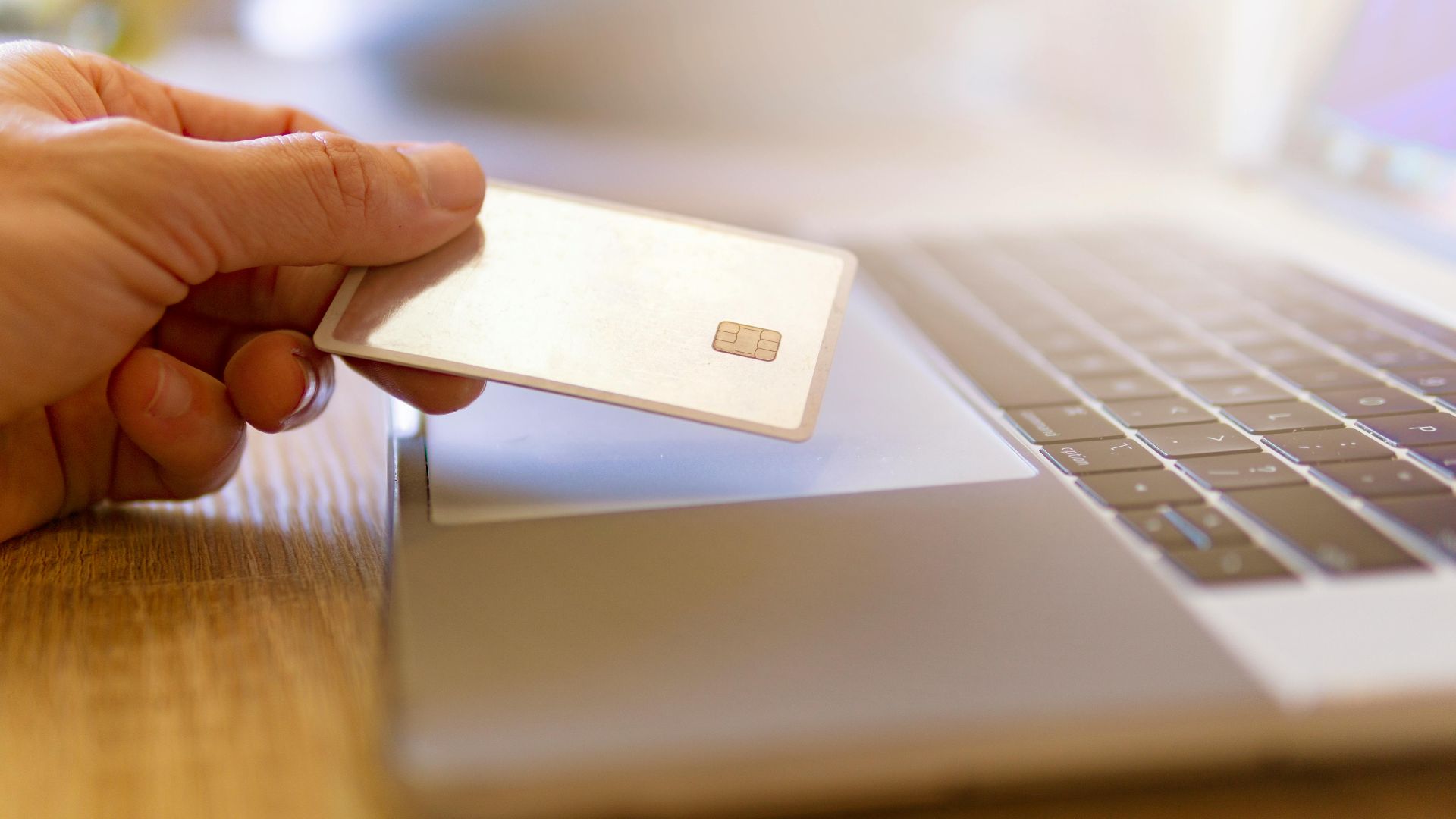 A person holds a credit card near a laptop for online shopping.