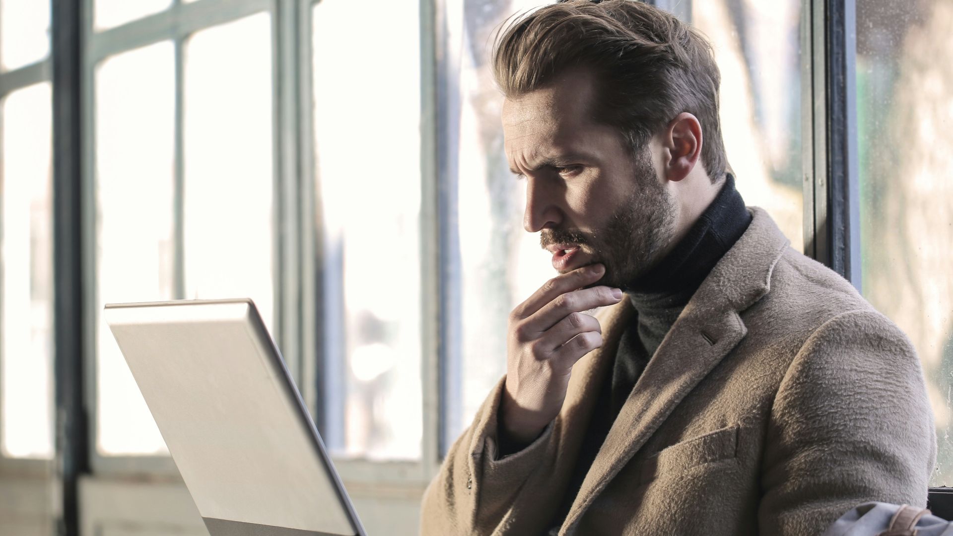 man holding his chin facing laptop computer