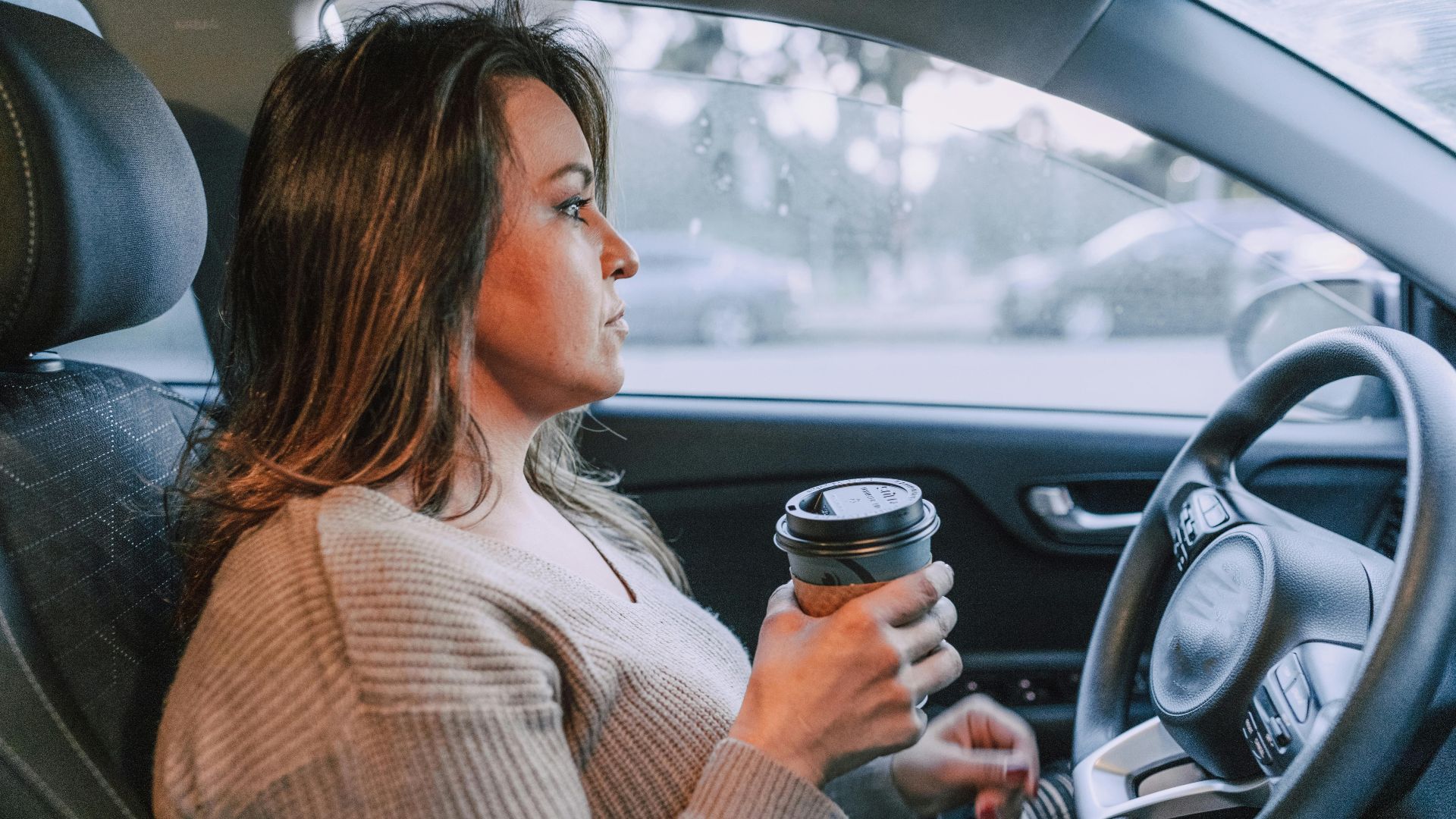 A woman in a car holding a disposable coffee cup, showing focus.