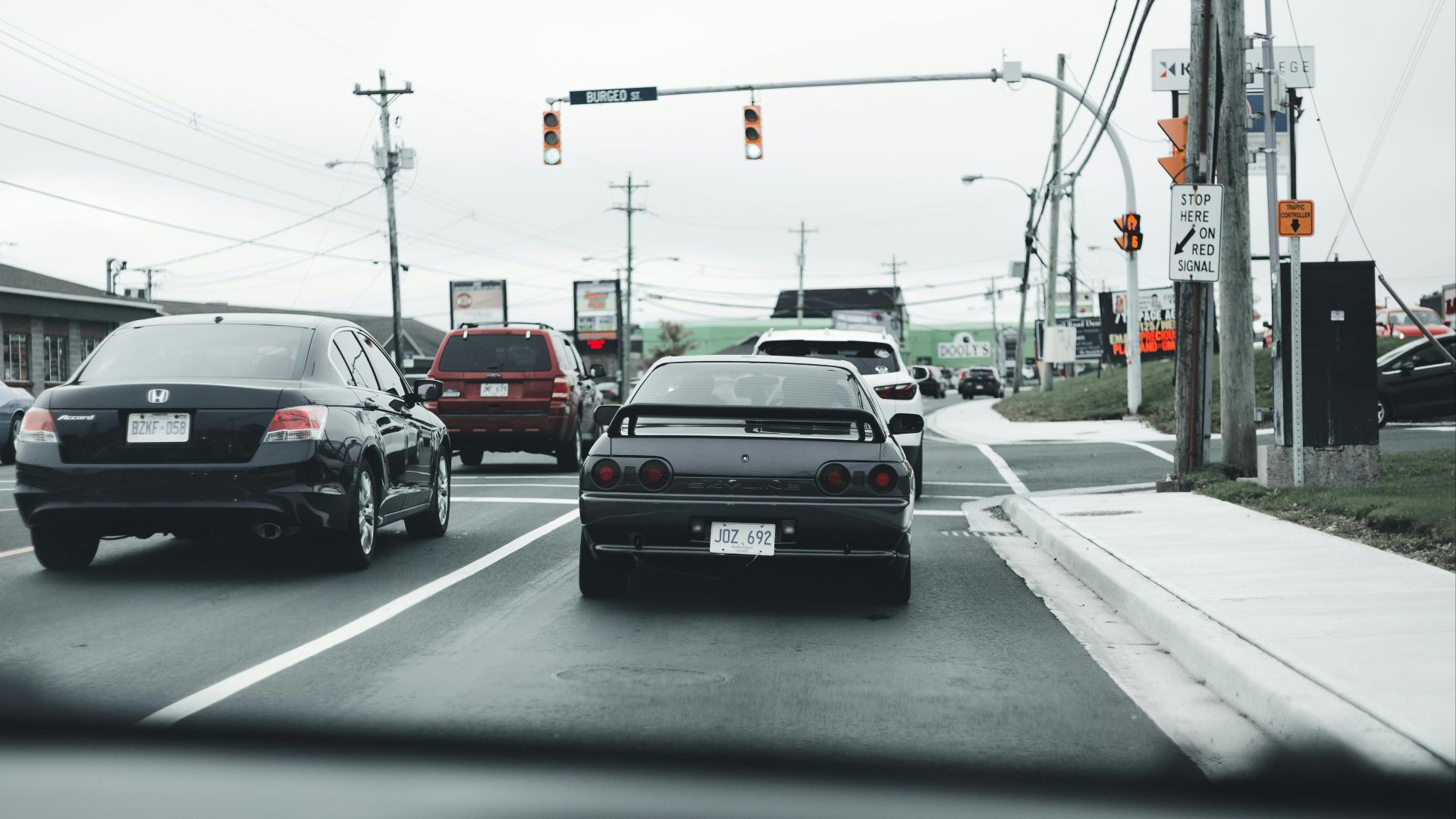 A busy road traffic scene with multiple cars and stop lights under cloudy skies.