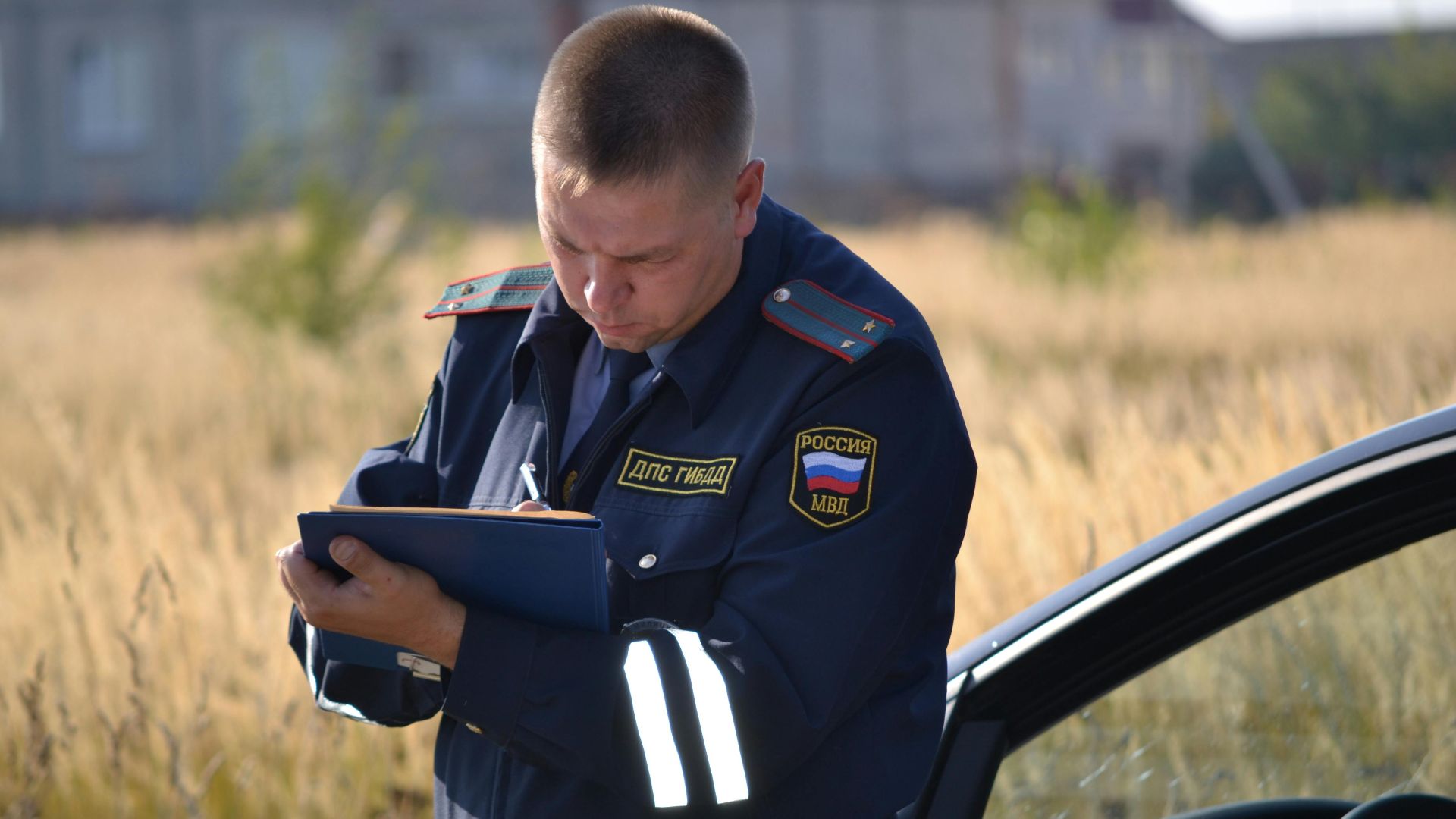 Police officer in uniform taking notes beside a car in a field.
