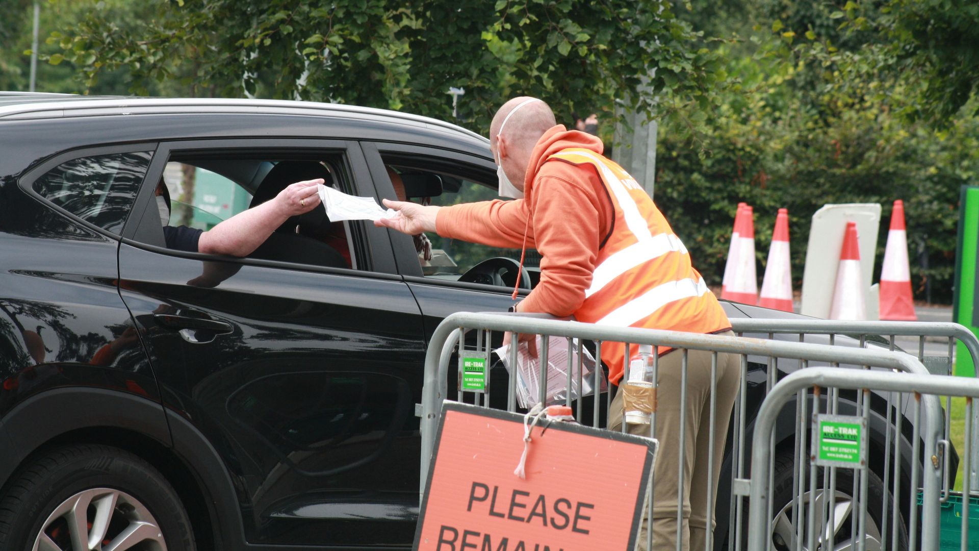 a man in an orange safety vest standing next to a black car