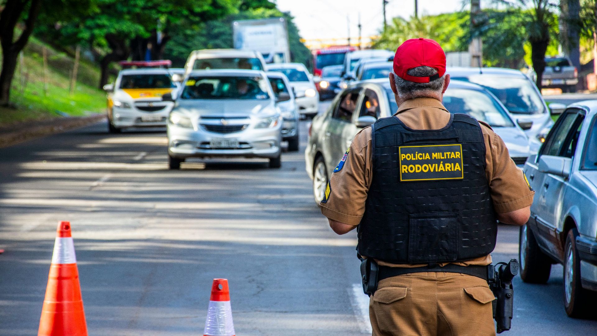 Police officer directing traffic in Londrina, Brazil with cars and cones on a busy street.