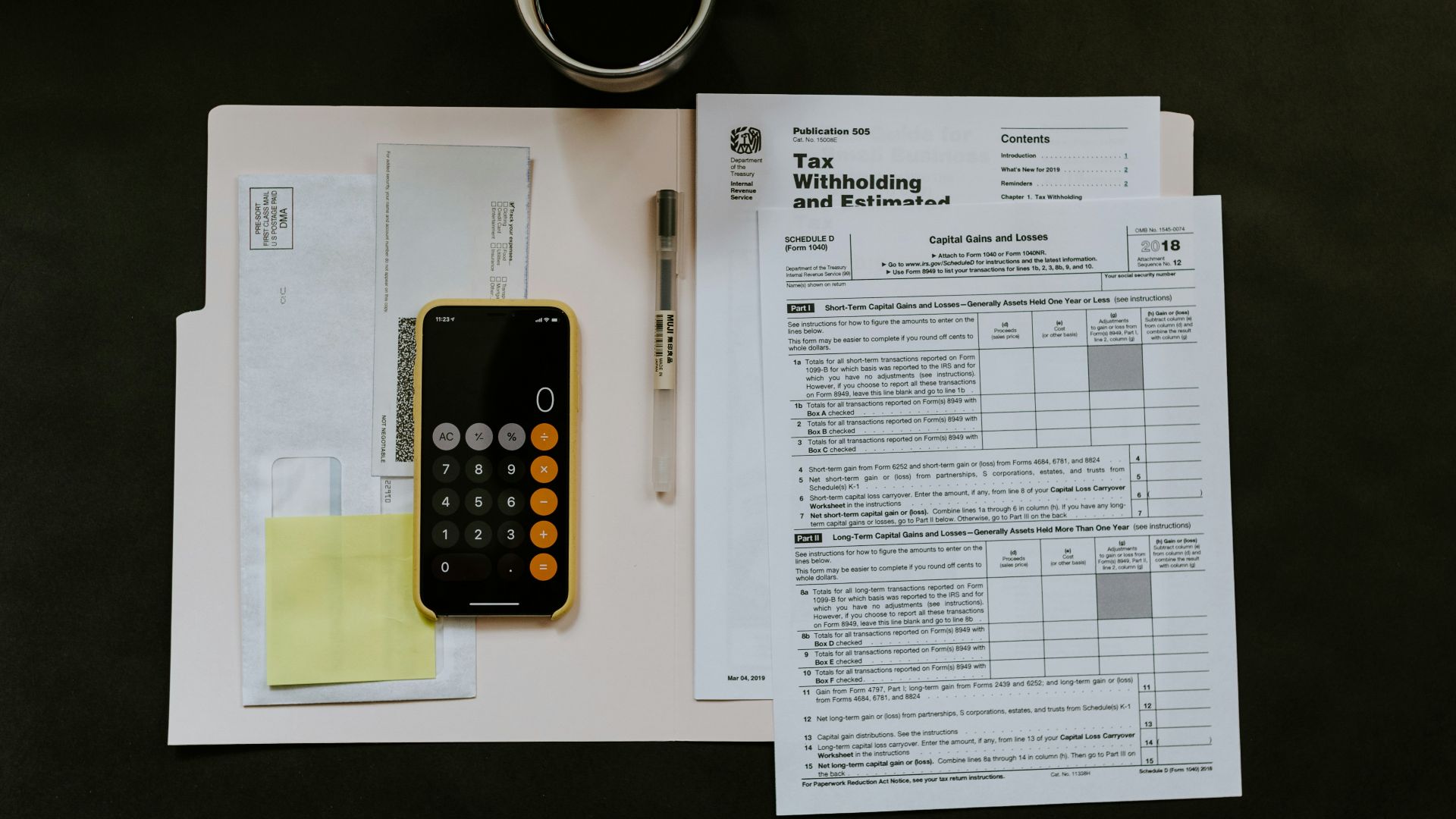 black Android smartphone near ballpoint pen, tax withholding certificate on top of white folder