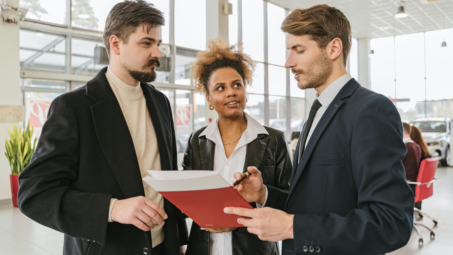 Business professionals discussing a car lease or purchase agreement in a showroom setting.
