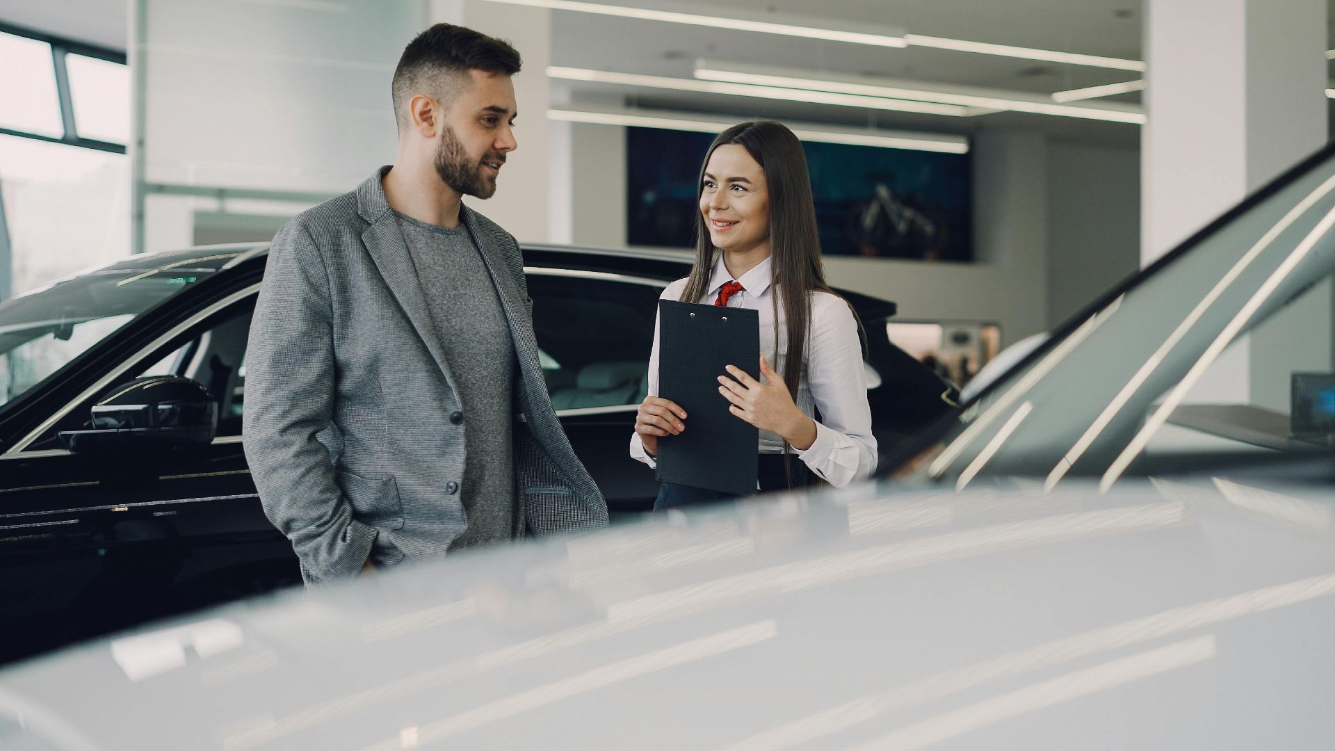 Man consults with salesperson in modern car dealership showroom.