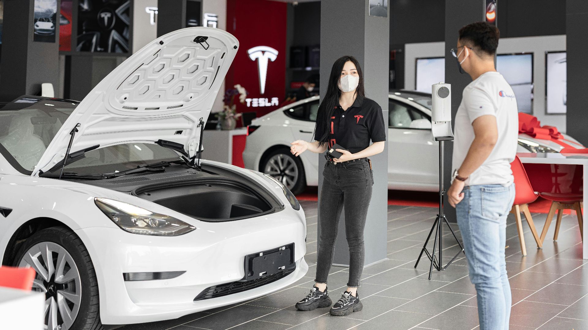 A customer talks with a sales representative about a Tesla Model 3 in a car dealership, showcasing the electric car's features.