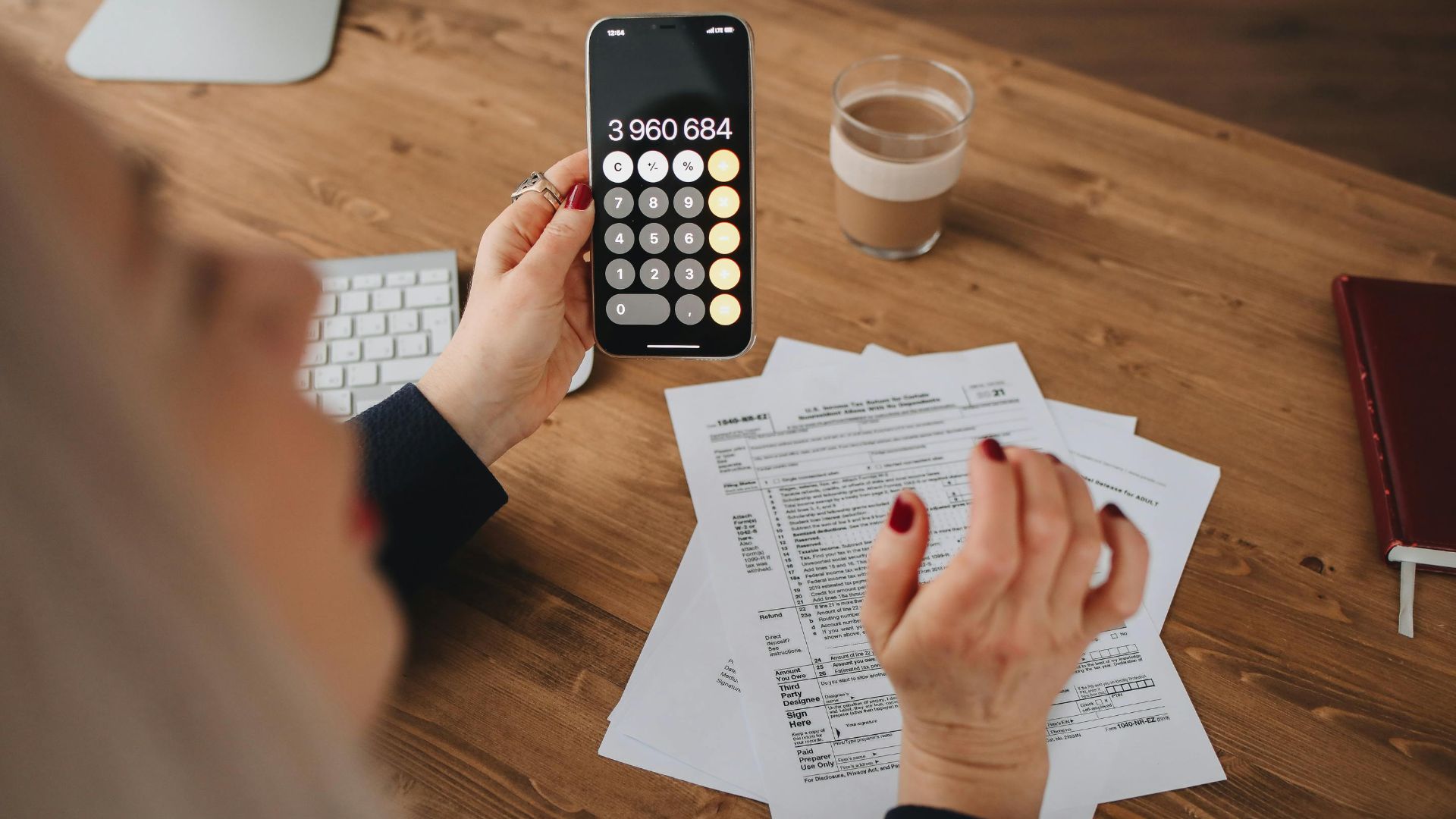 A woman calculates on her smartphone while working with documents at a desk.