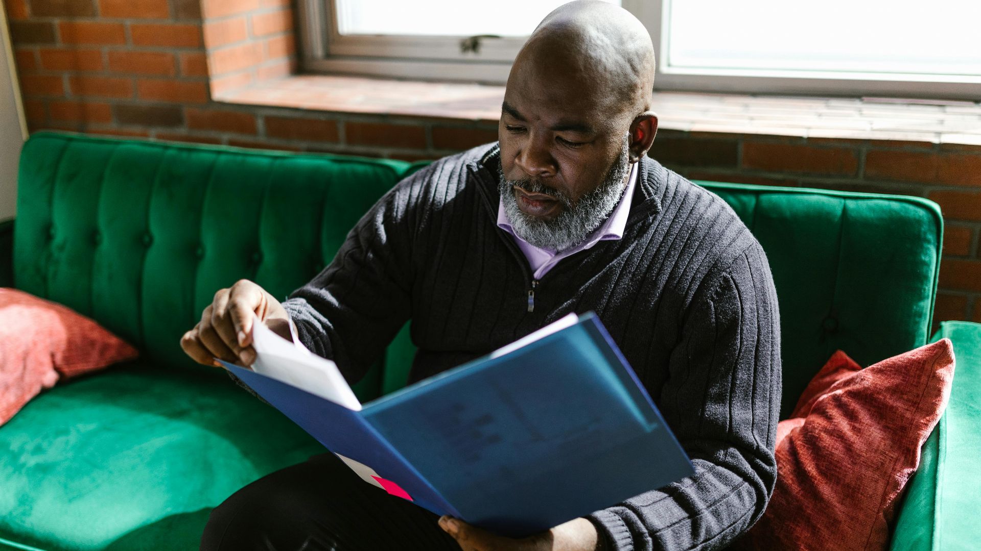 African American adult man reviewing documents on a green sofa, indoors.