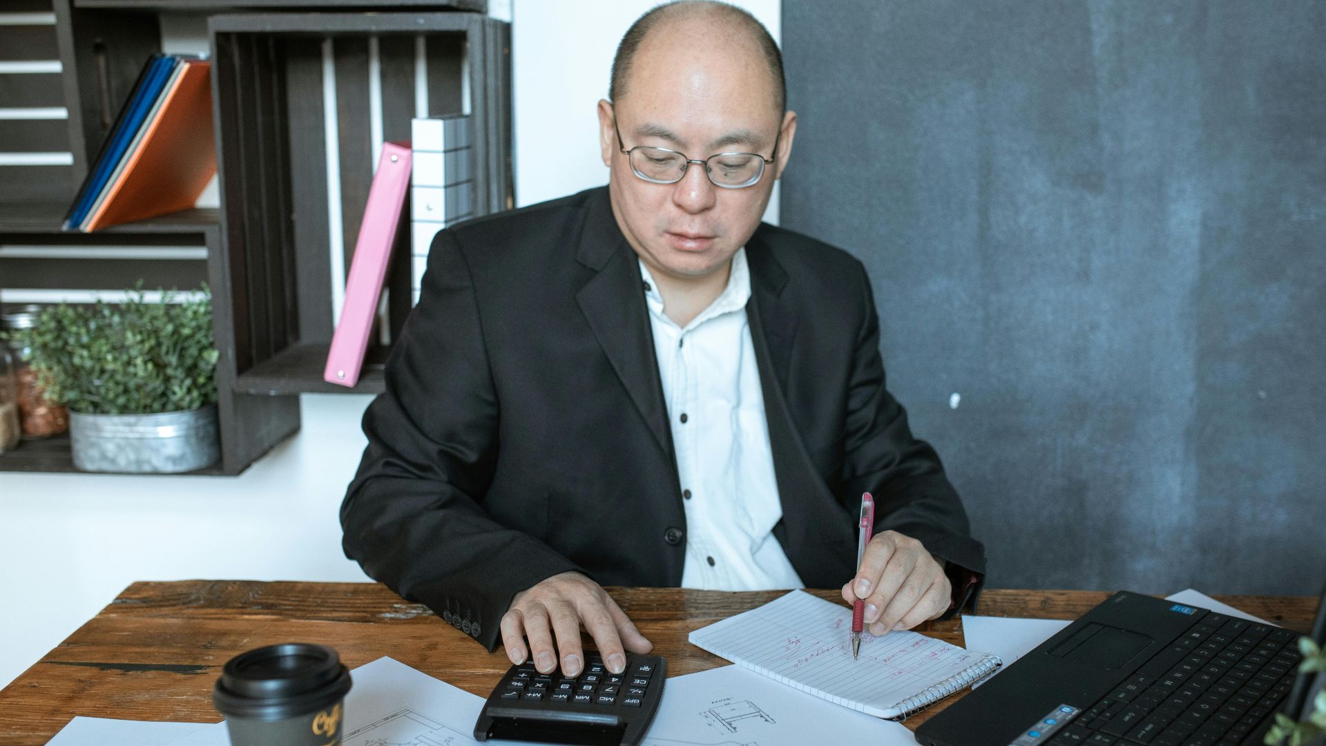 Asian businessman working with calculator and notes at his desk in a modern office space.