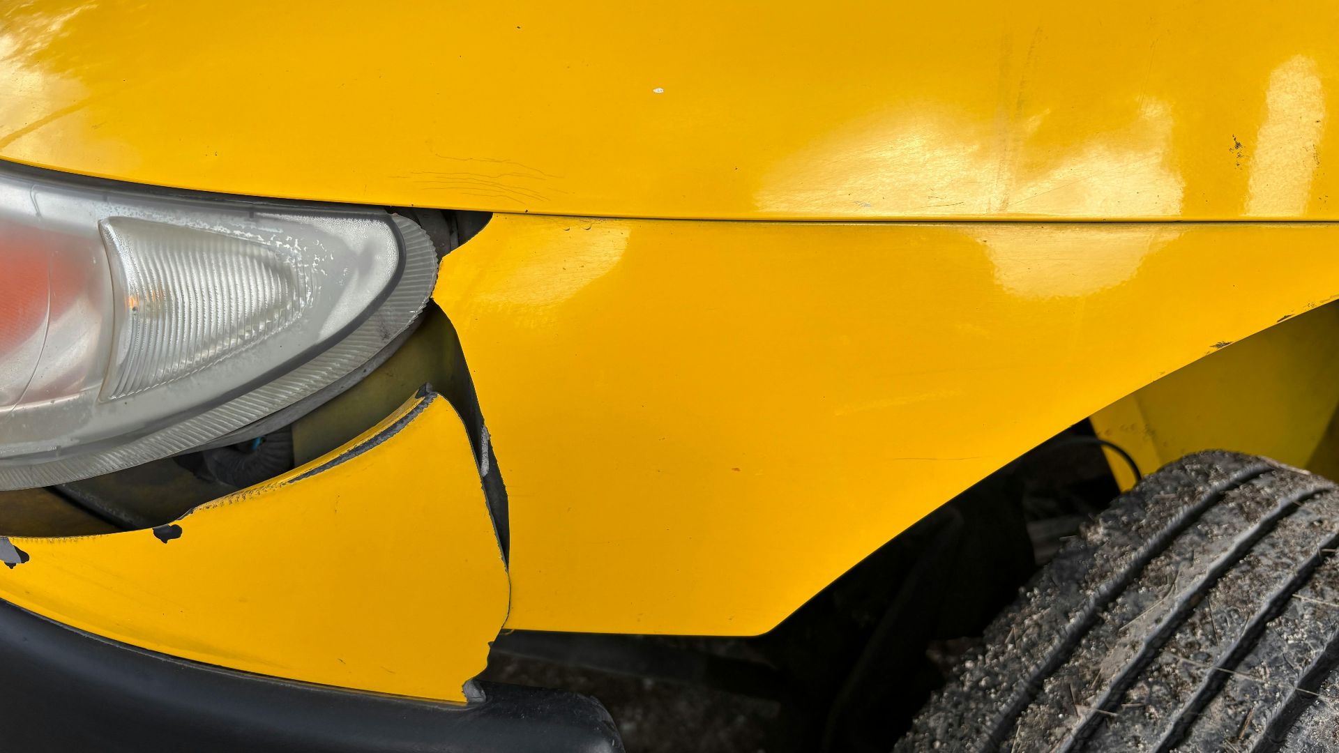 Close-up image of a yellow car's damaged front bumper and headlight for insurance or accident concept.