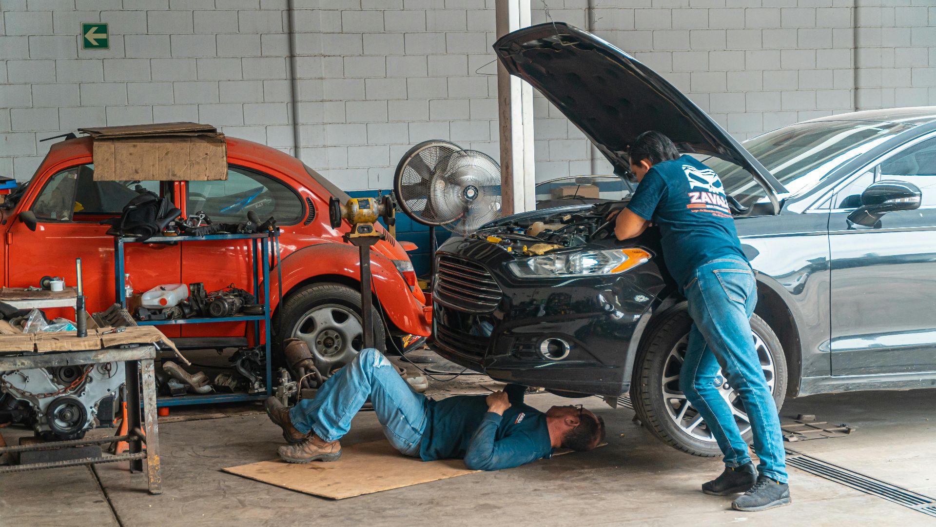 Mechanics working in an automotive workshop, repairing cars and performing maintenance.