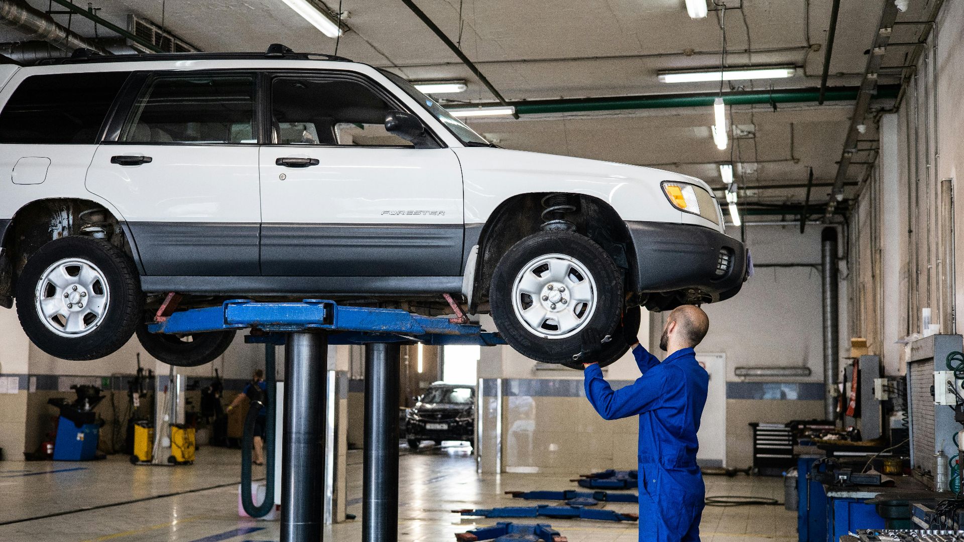 A mechanic inspecting a white SUV lifted in a well-lit auto repair shop.