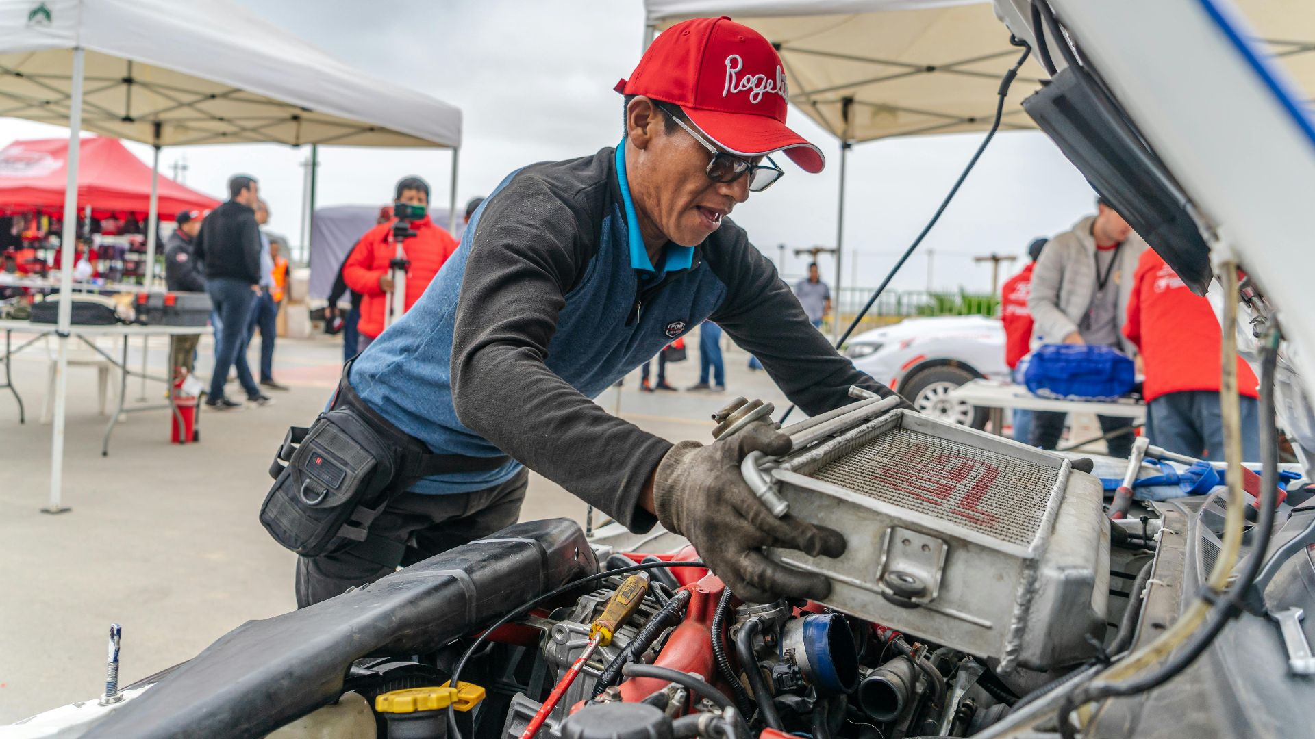 Mechanic examining car engine during an outdoor automotive event. Focus on auto repair.