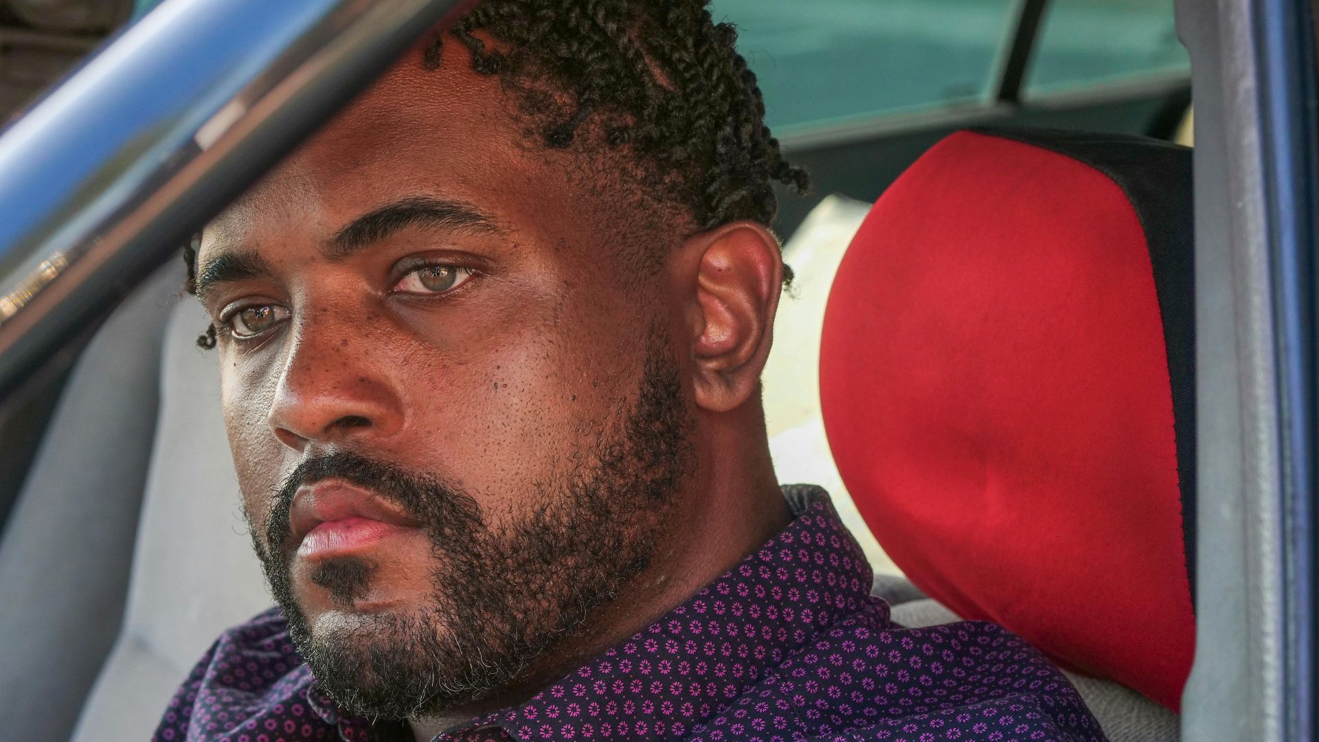 Close-up portrait of a man with facial hair sitting in a car staring intently.