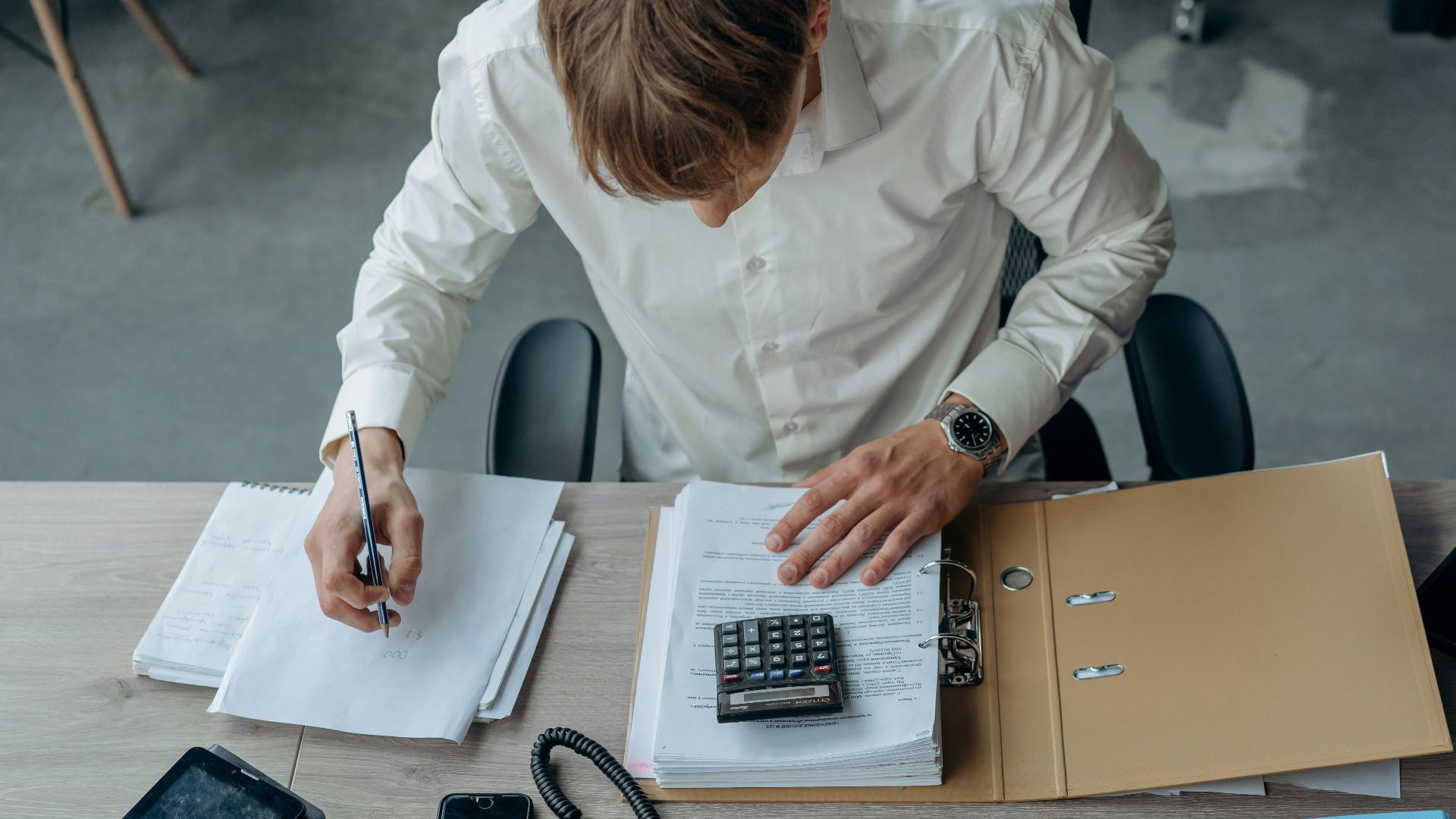 Man in an office reviewing financial papers with a calculator on a desk.