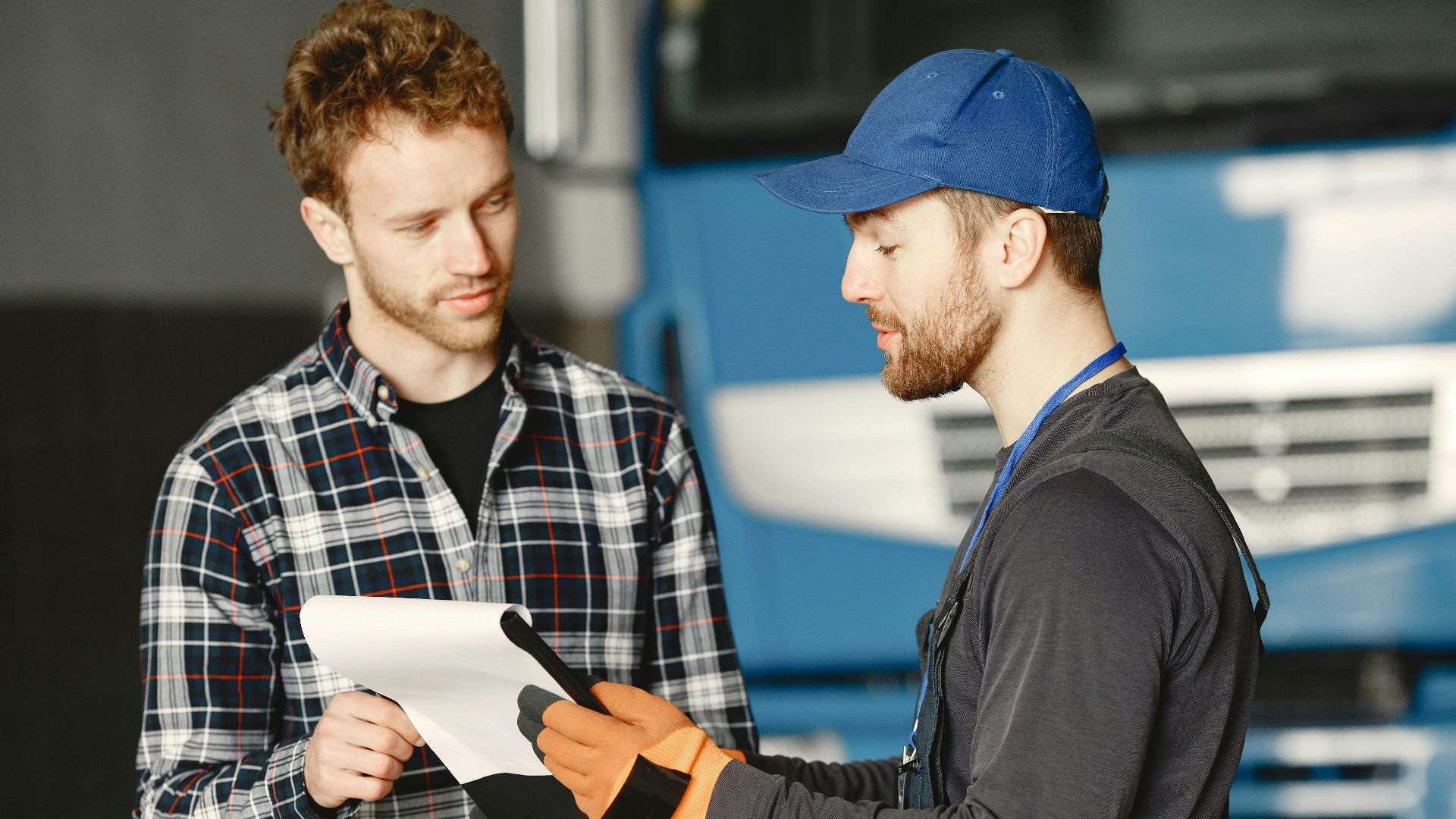Mechanic in uniform talks with a customer about vehicle maintenance inside a garage.