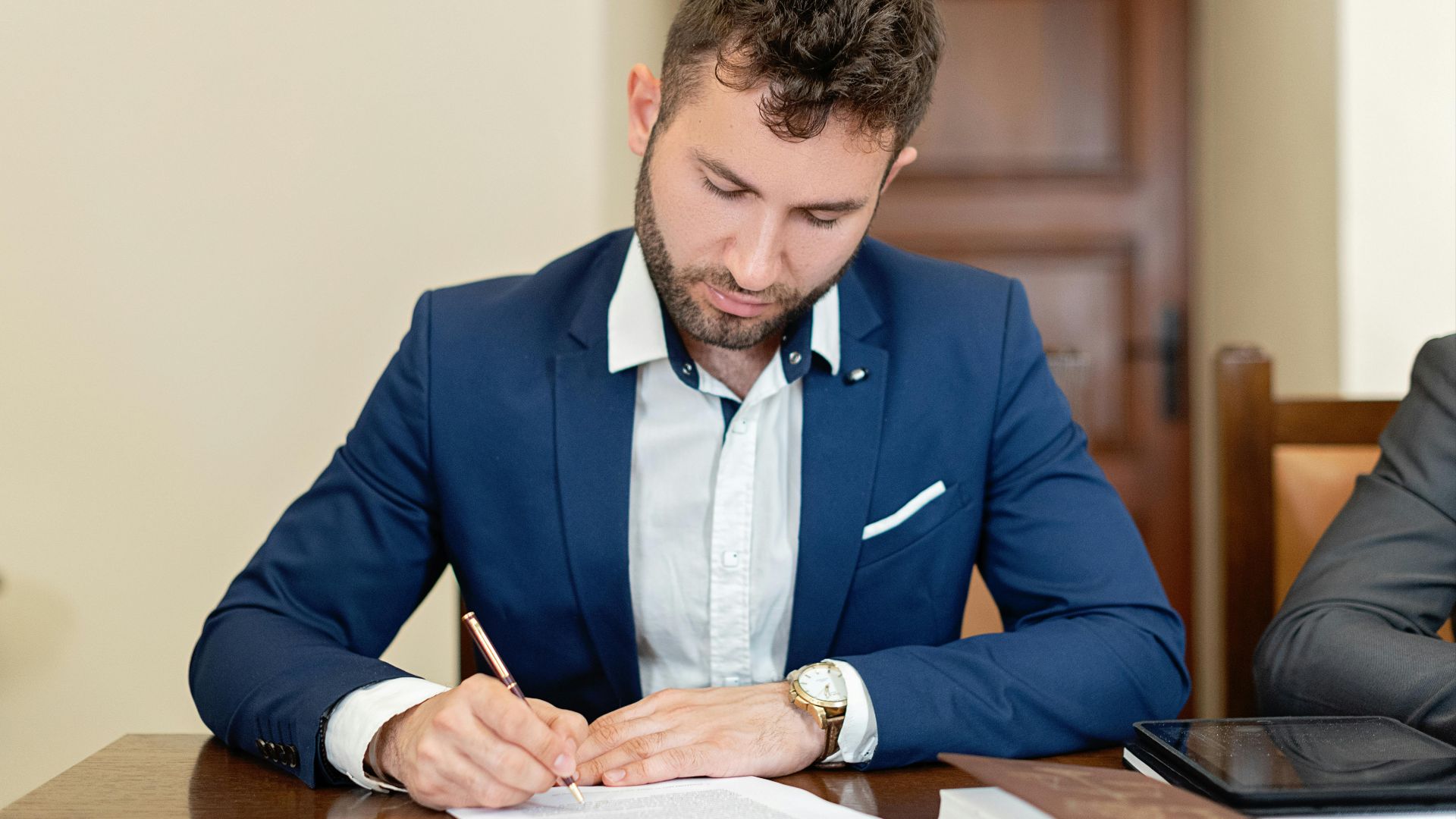 Confident businessman in a suit signing a contract at the office desk.