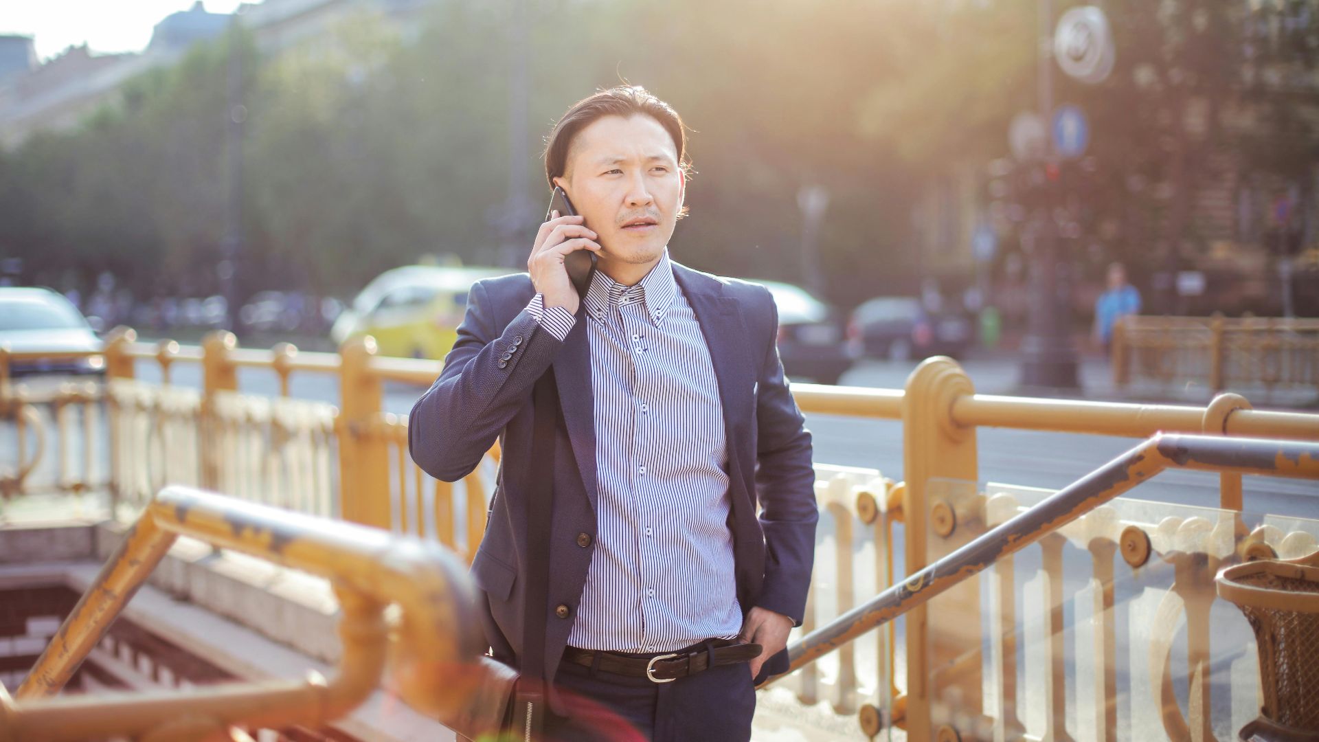 Confident Asian man in business attire making a phone call outdoors on a sunny day.