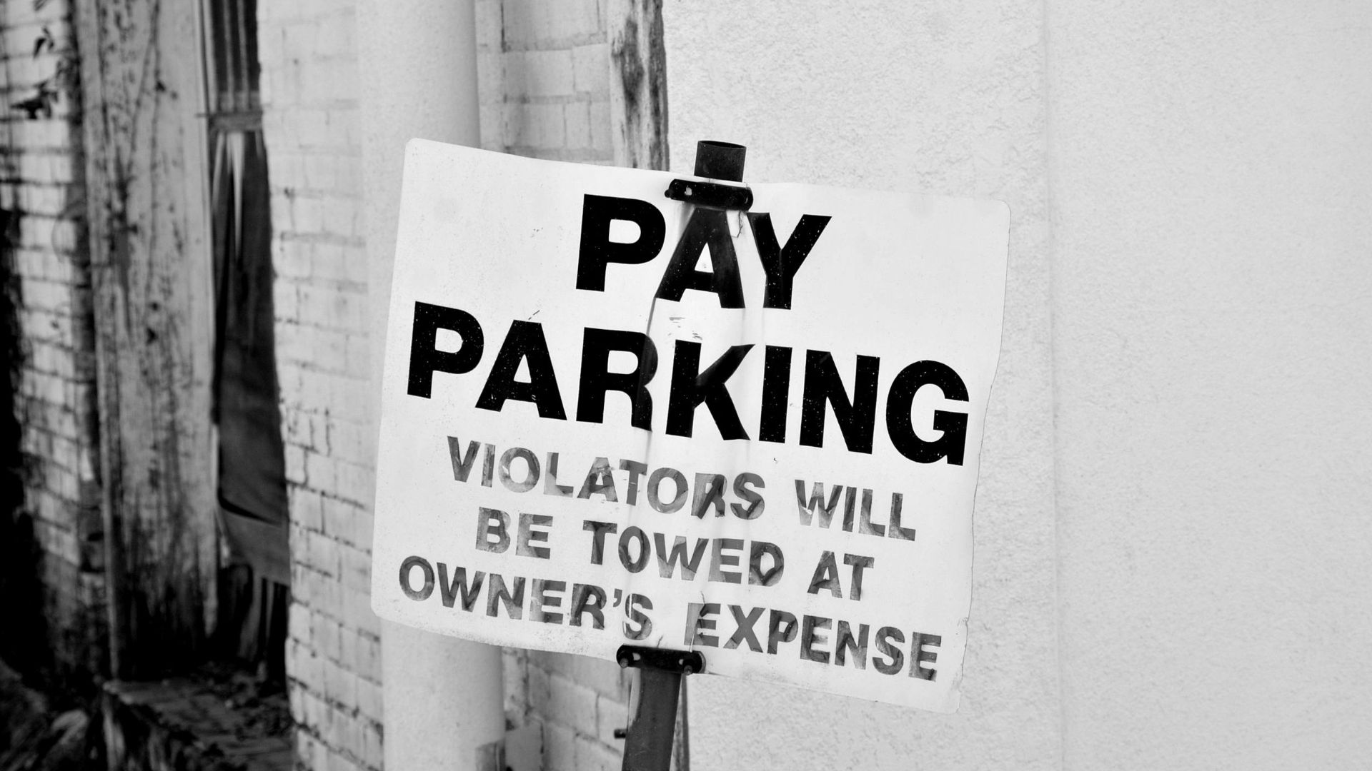 A black and white photo of a pay parking sign in downtown Tyler, Texas. Violators will be towed.