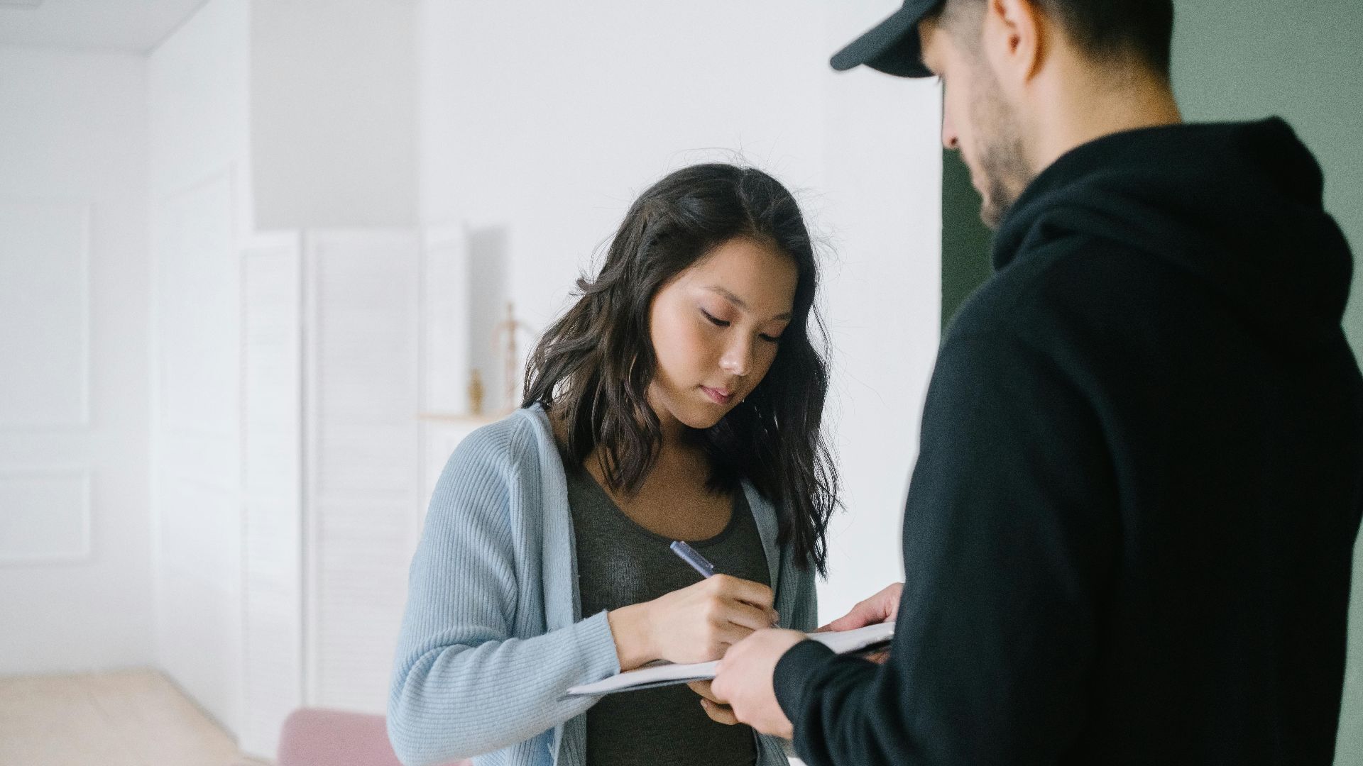 Woman signing for a package delivered by courier at home interior.