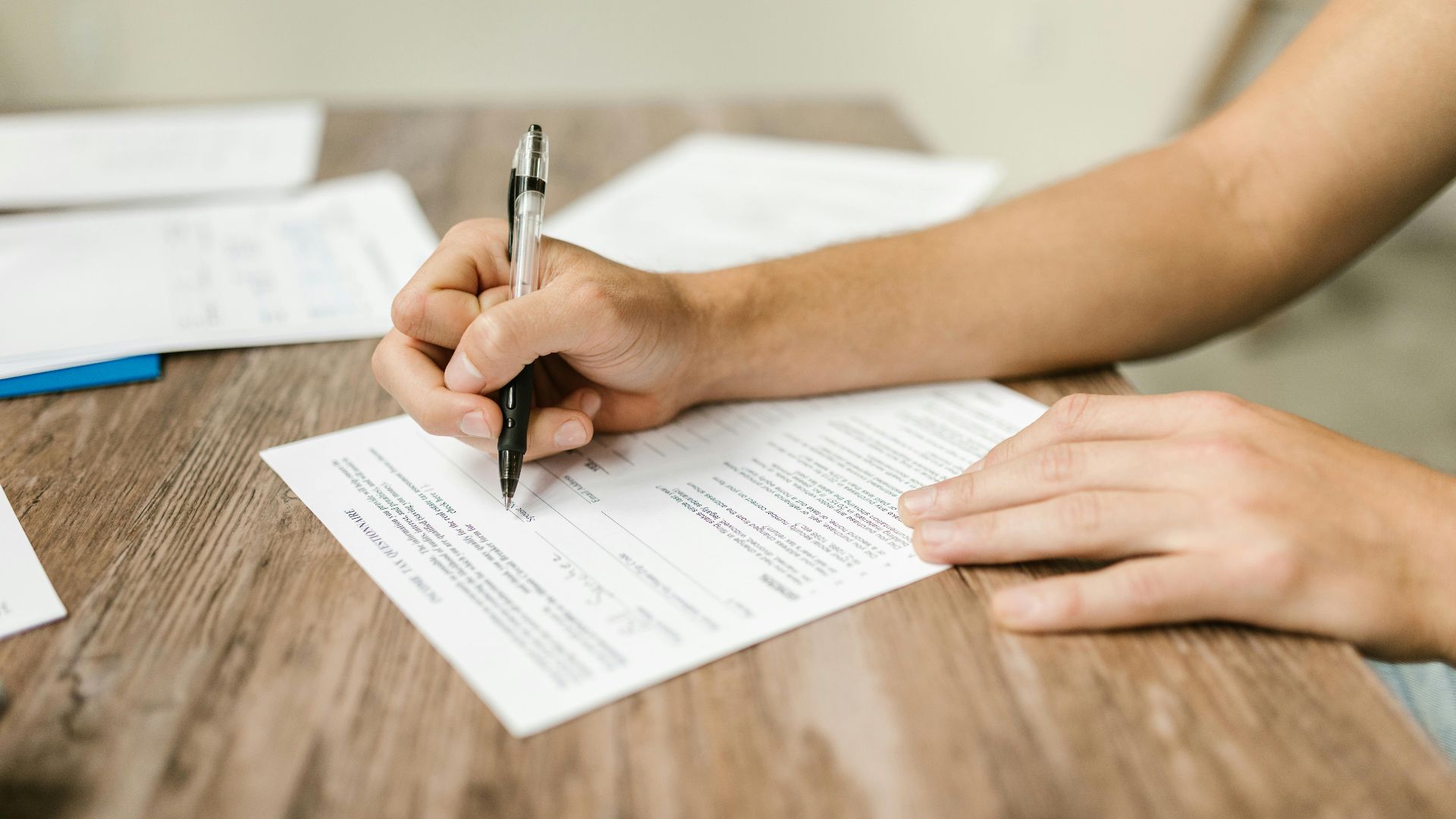 Hand filling out paperwork with a pen, showcasing focus on document completion.