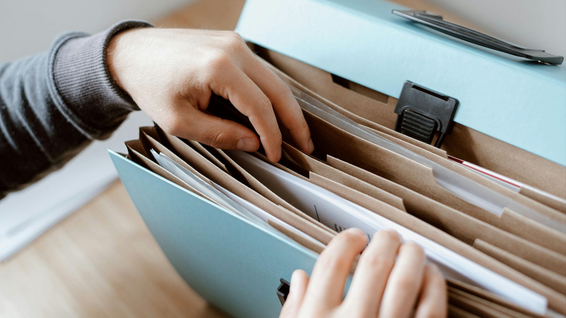 Crop unrecognizable person selecting document in opened briefcase for documents placed on wooden table